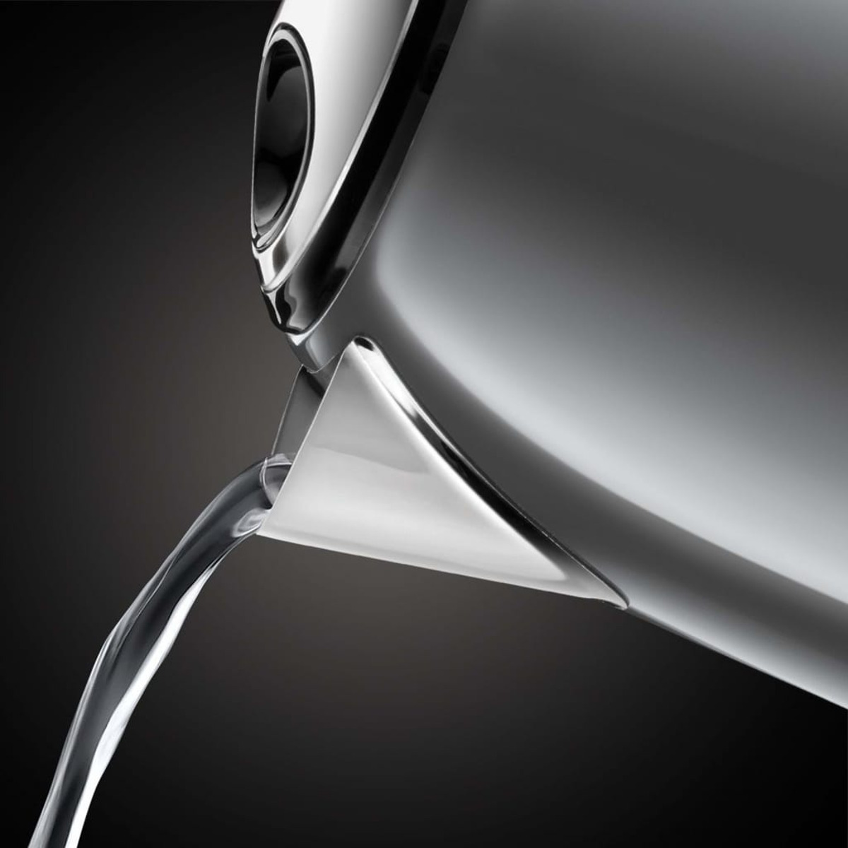 Srebrny czajnik wylewający strumień wody na ciemnym tle.