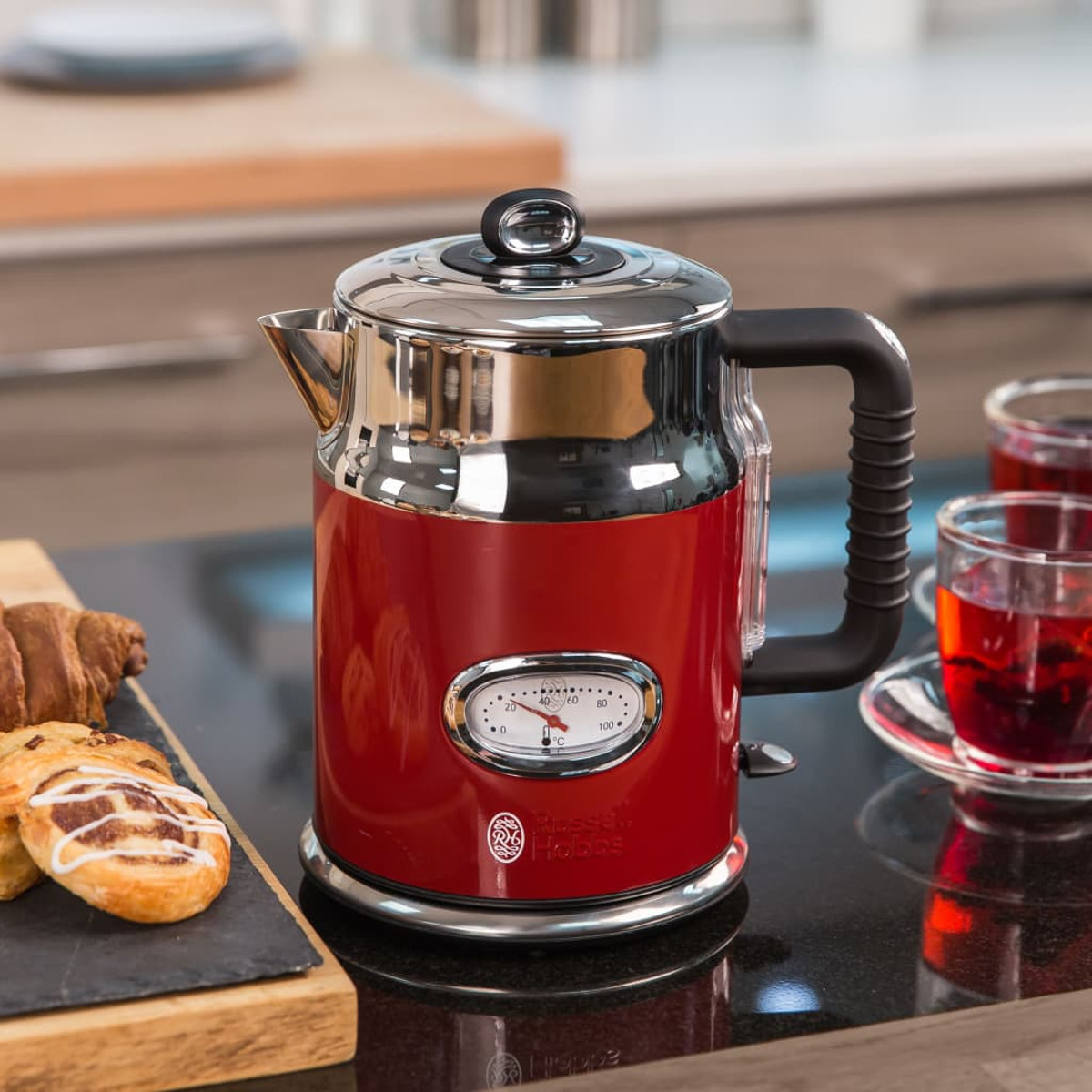 Roter Russell Hobbs Wasserkocher mit Temperaturanzeige, Croissants und Gebäck auf schwarzer Theke.