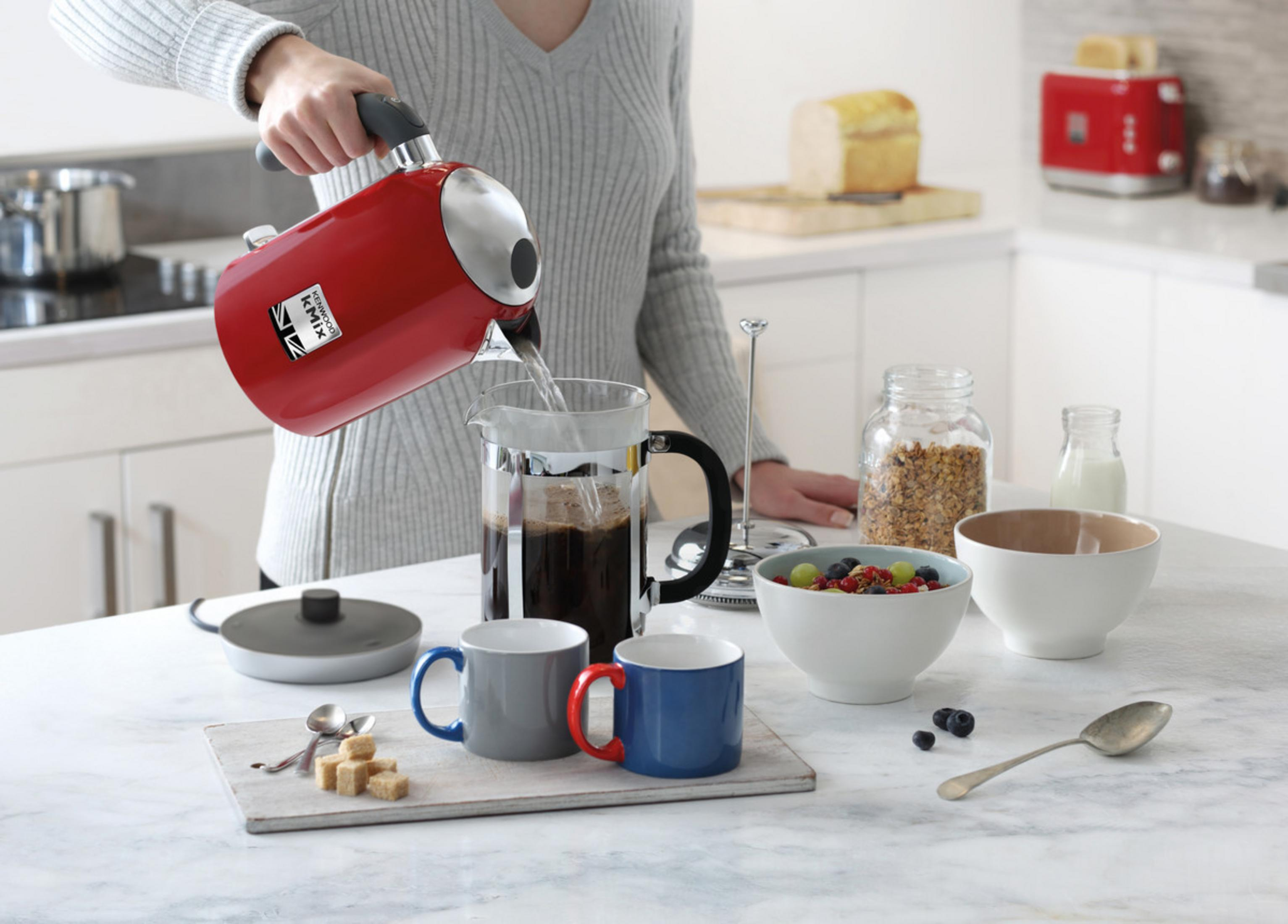 Osoba nalewa wodę z czerwonego czajnika do prasy francuskiej. Kuchnia.