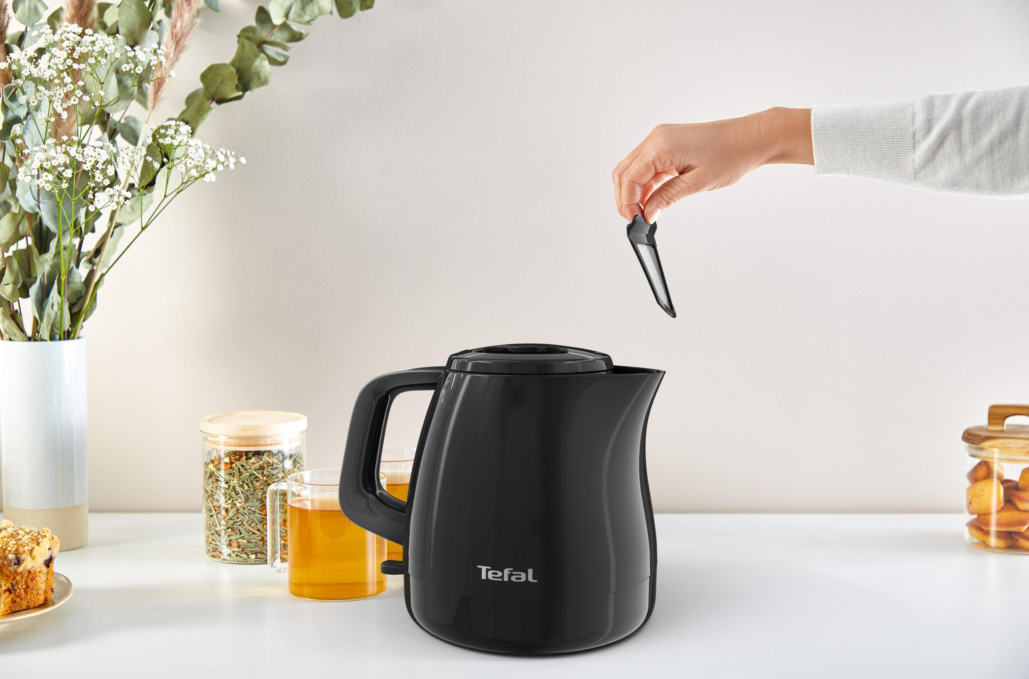 Schwarzer Wasserkocher, Hand entfernt Filter. Weitere Gegenstände sind sichtbar, darunter eine Tasse Tee.