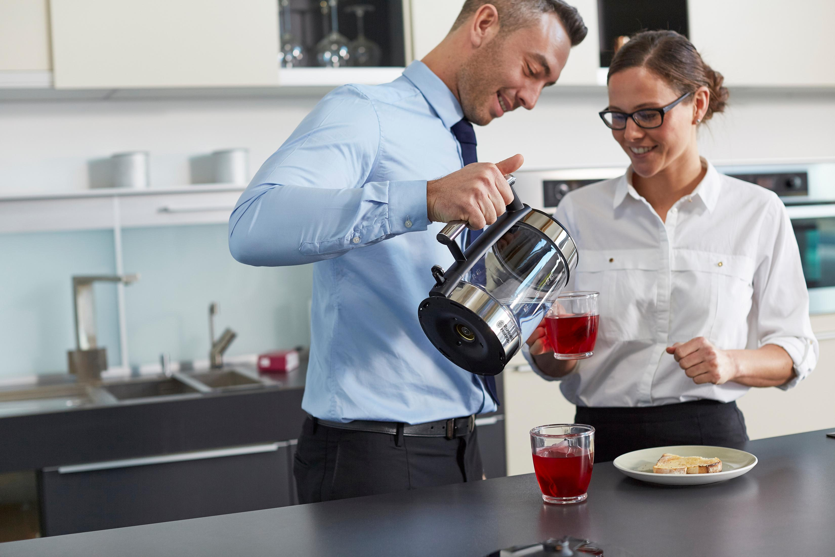 Ein Mann gießt Tee in ein Glas, eine Frau hält ein anderes Glas, Küchenhintergrund.