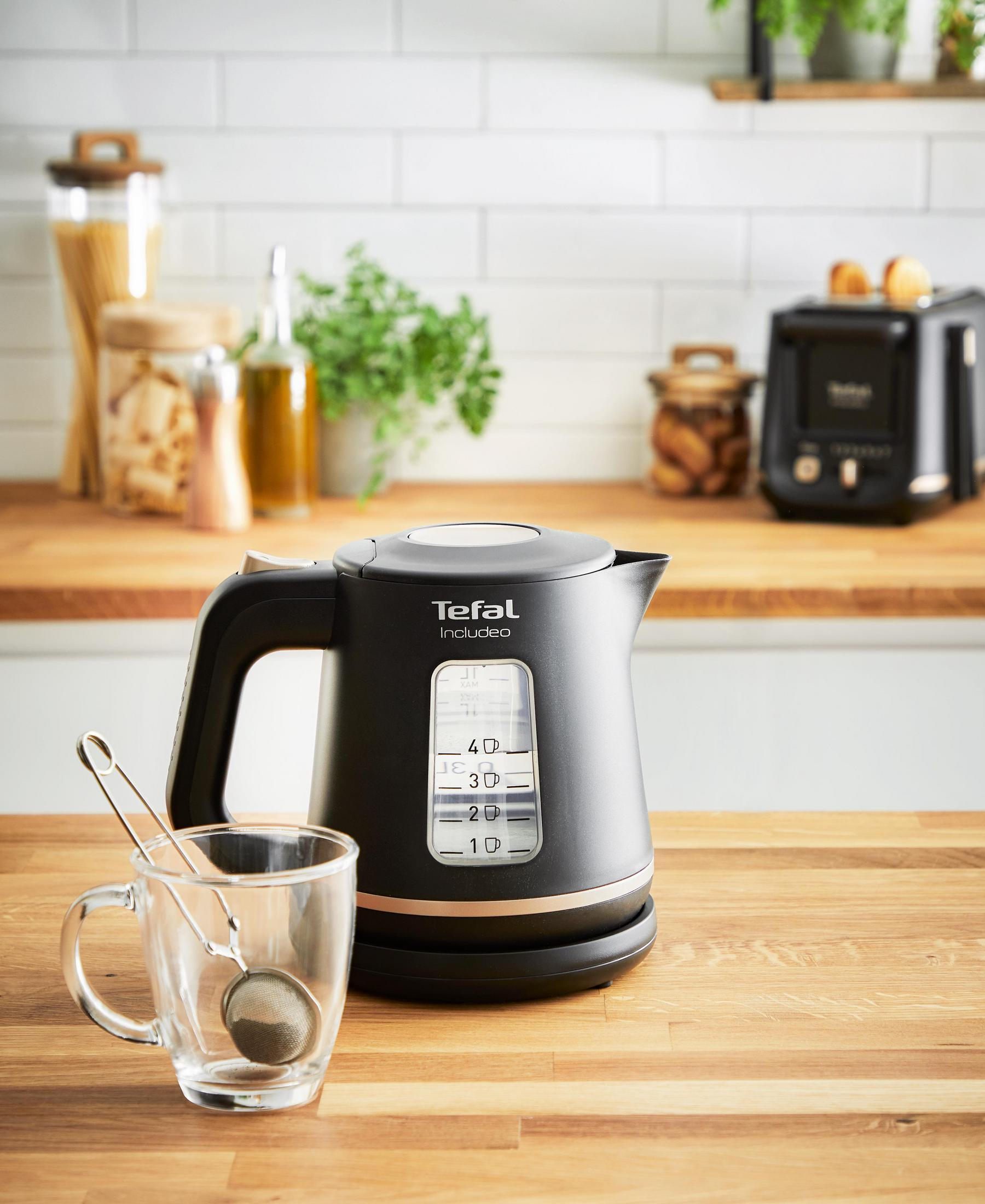 Czarny czajnik elektryczny i filiżanka herbaty z zaparzaczem do herbaty na drewnianym stole.