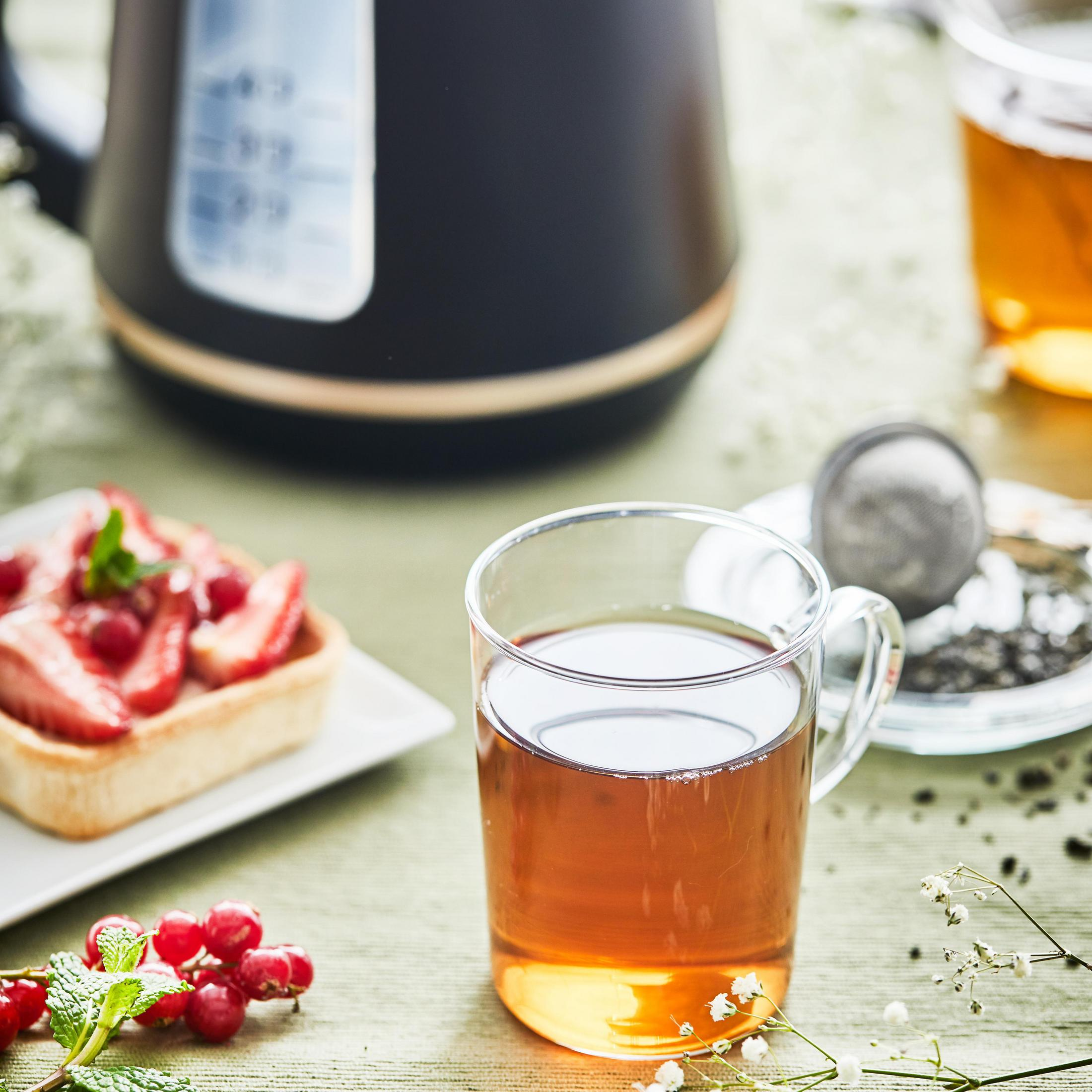 Szklanka herbaty z tartą i jagodami oraz czajnik na stole, tworząc martwą naturę.