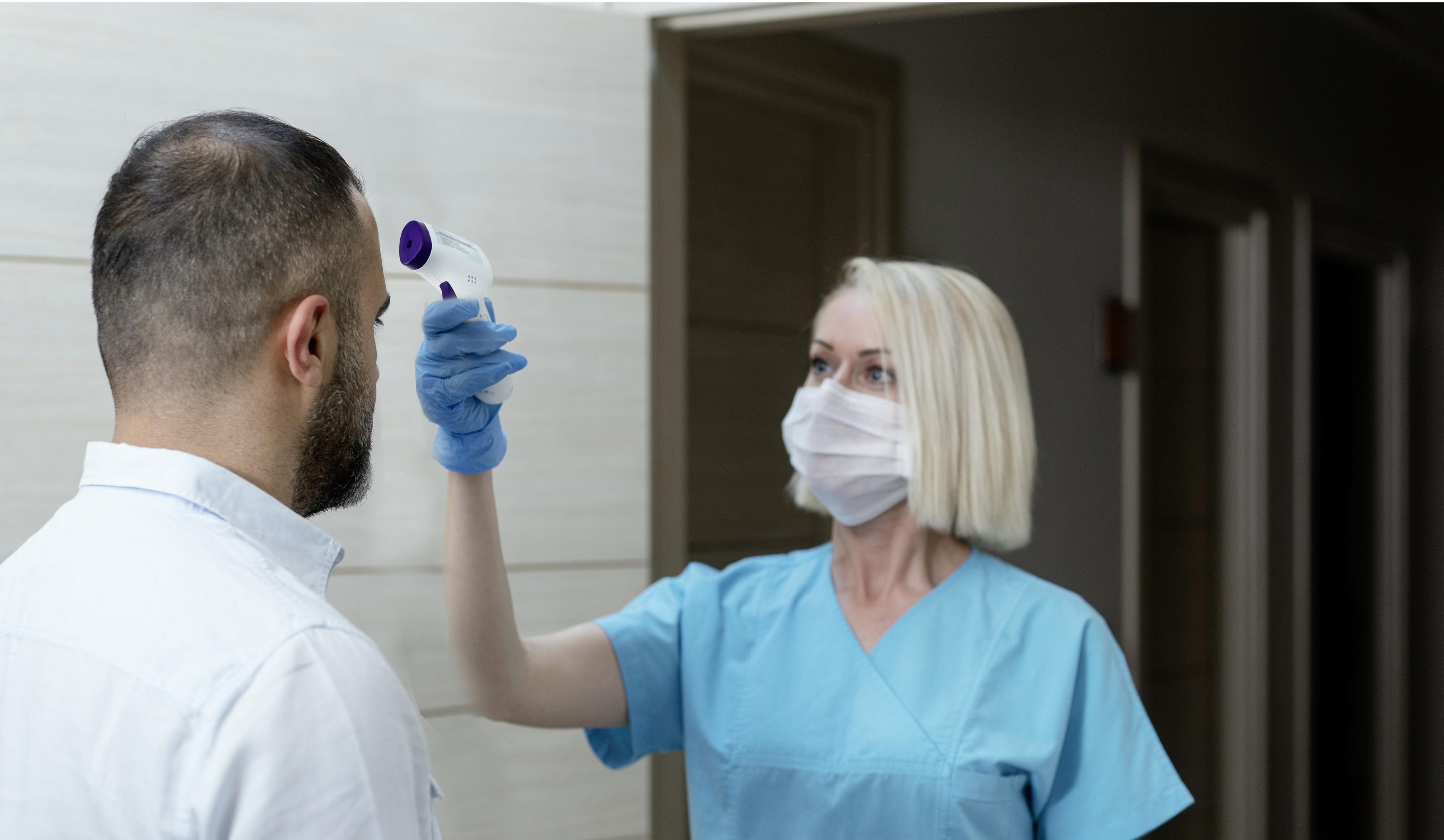 Eine medizinische Fachkraft misst die Temperatur einer Person mit einem Thermometer.