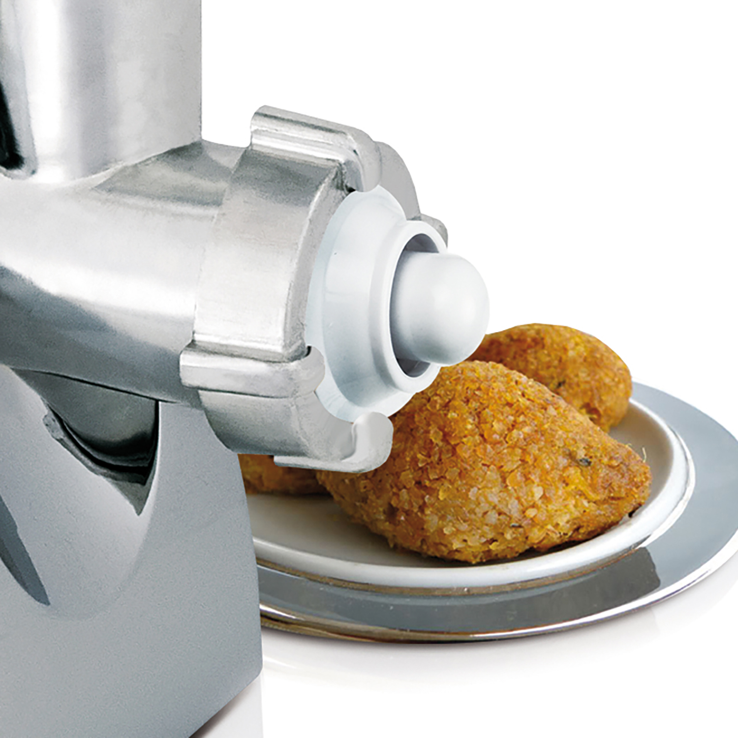 Picadora de carne. Un plato blanco con dos bolas de kibbeh fritas está frente a la boquilla de la picadora.