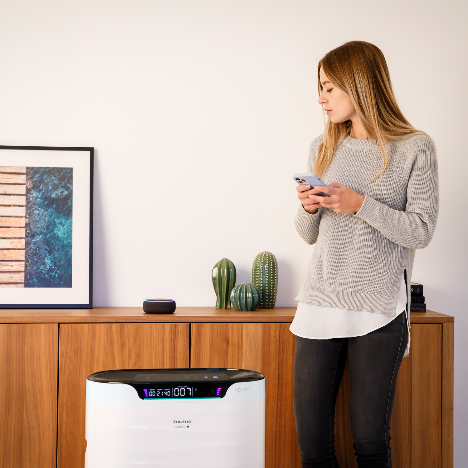 Una mujer junto a un mueble de madera con un purificador de aire y un altavoz inteligente.