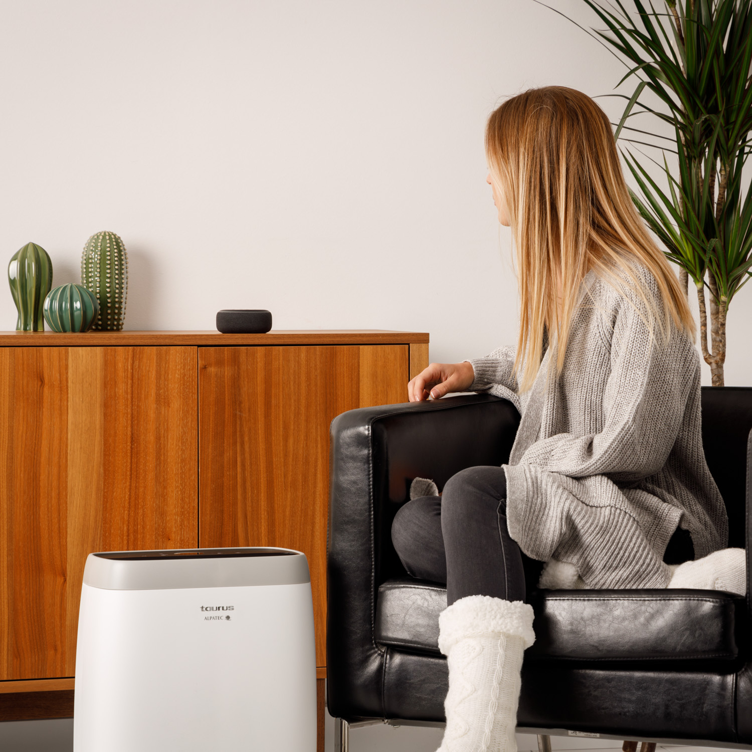 Mujer en una habitación con altavoz inteligente, purificador de aire y mueble de madera.