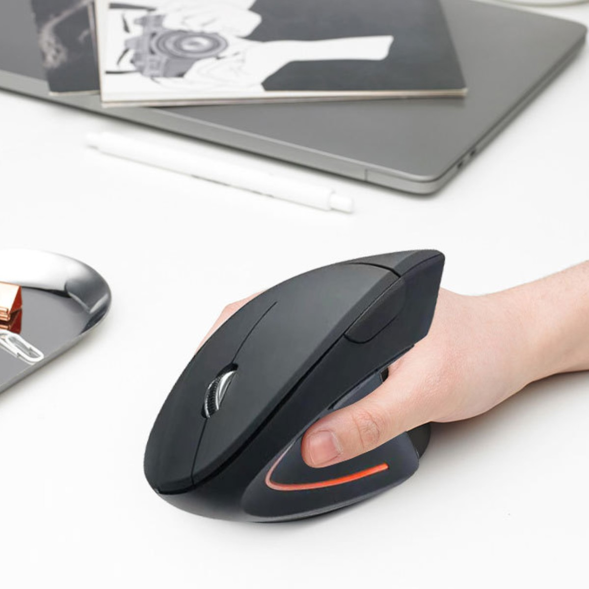 Eine schwarze ergonomische Maus auf einem weißen Schreibtisch. Ein Laptop und Stift sind sichtbar.