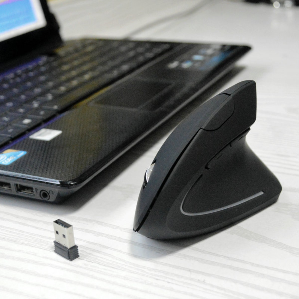 Eine schwarze vertikale Maus mit USB-Empfänger und Laptop.
