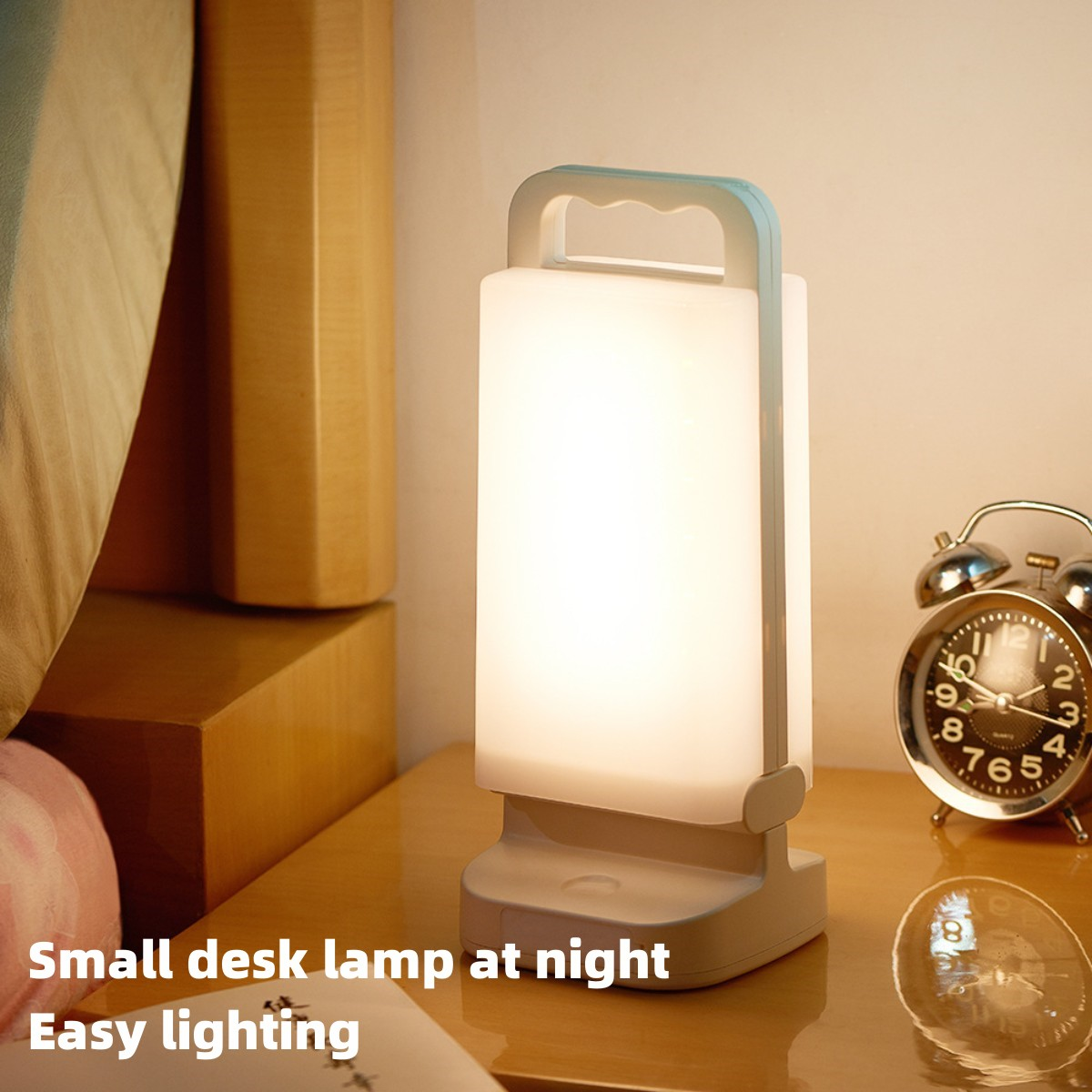 Kleine Schreibtischlampe auf einem Nachttisch neben einem analogen Wecker. Warmes Licht.