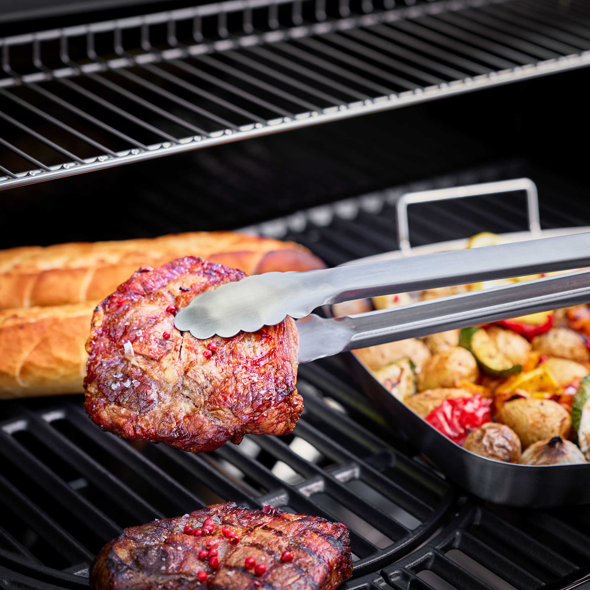 Gegrilltes Steak mit Zangen, Gemüse und Brot auf einem Grill.