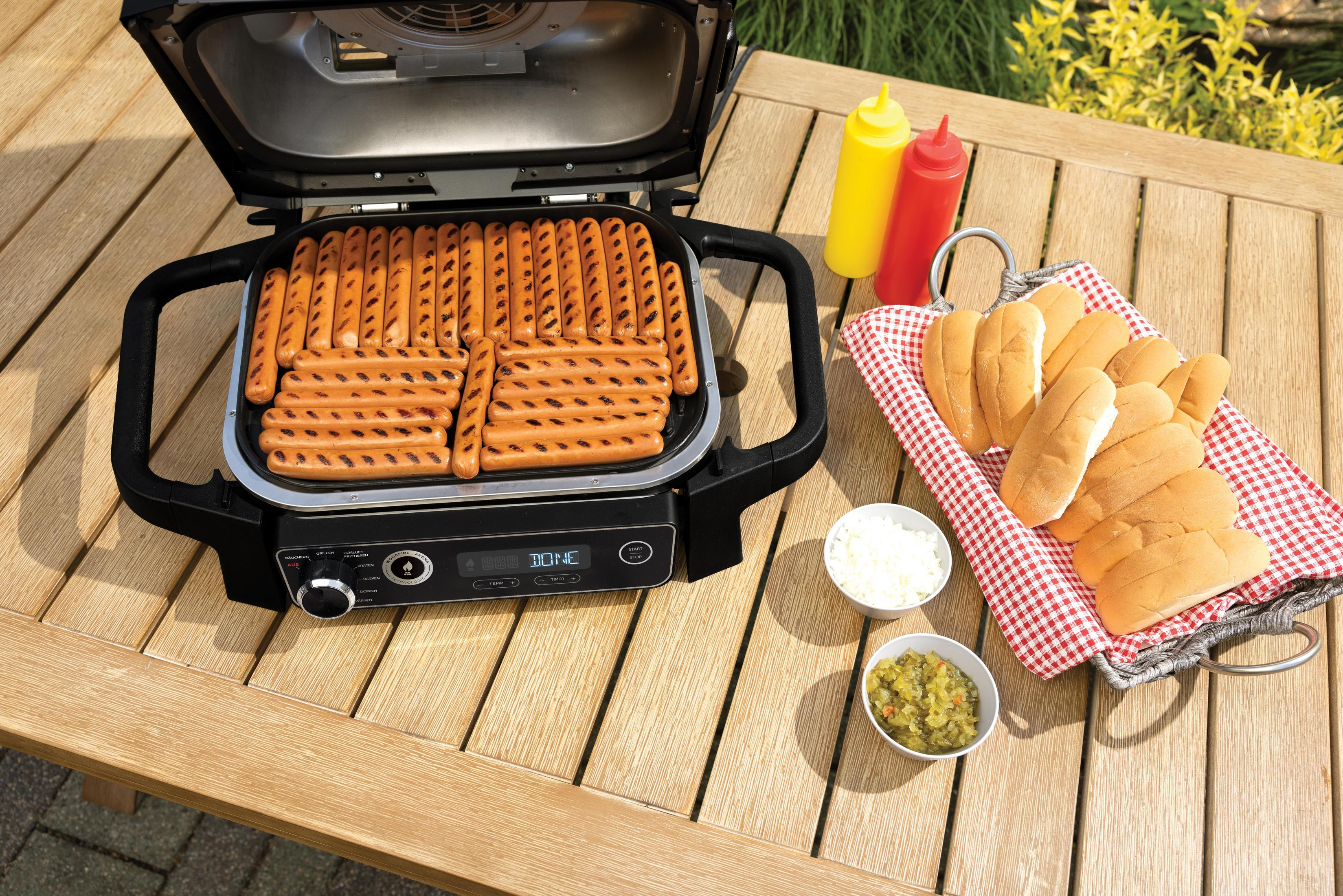 Grill met hotdogs, broodjes en kruiden. Houten tafel met grill, gele mosterd, rode ketchup en kommen.