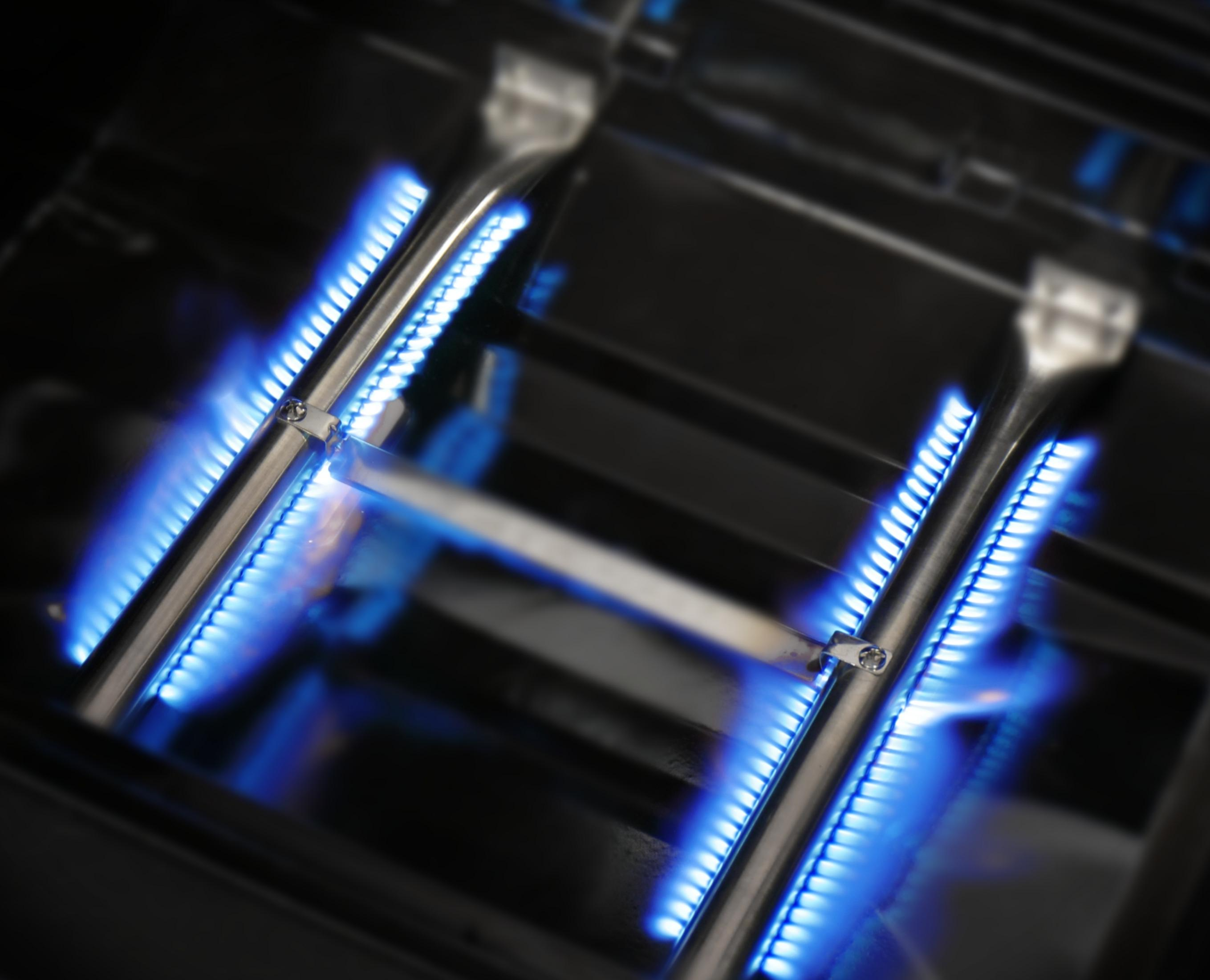 Nahaufnahme eines Gasgrills. Blaue Flammen sind von den Brennern sichtbar, Metallteile gezeigt.