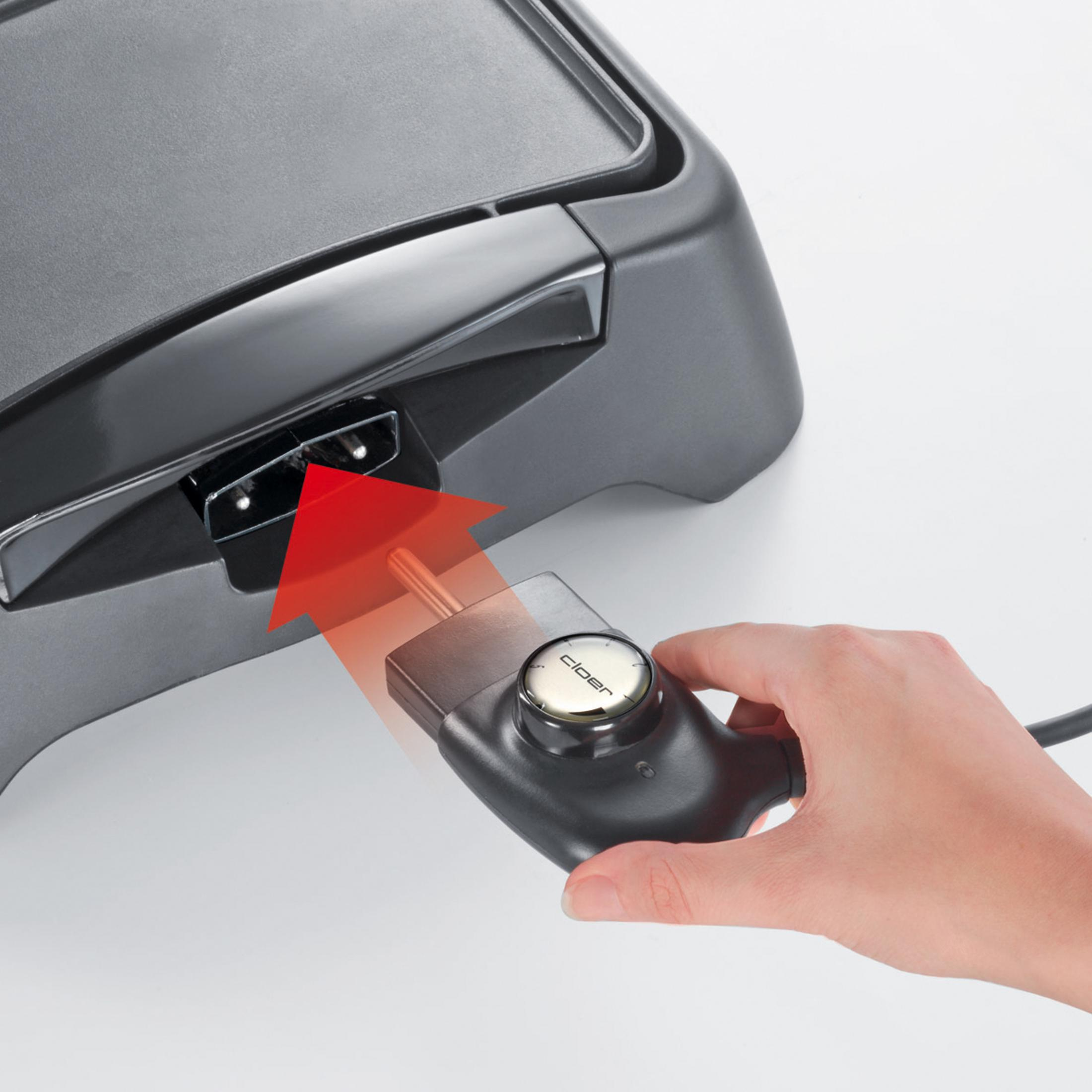 Eine Hand, die ein Kabel in eine schwarze Elektro-Griddle einsteckt.