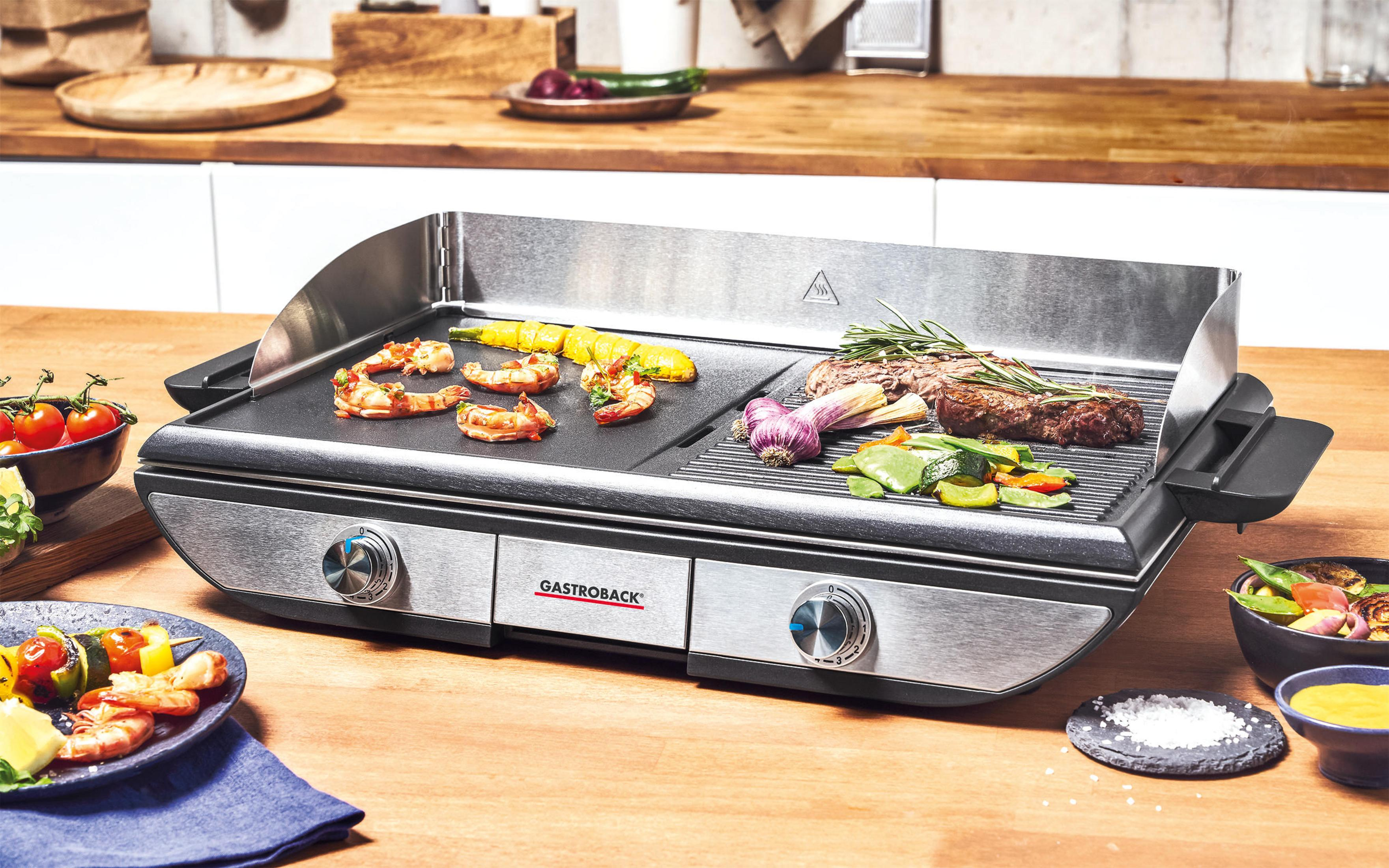 Ein Edelstahlgrill mit gekochtem Essen. Garnelen, Mais, Steak und Gemüse sind sichtbar.