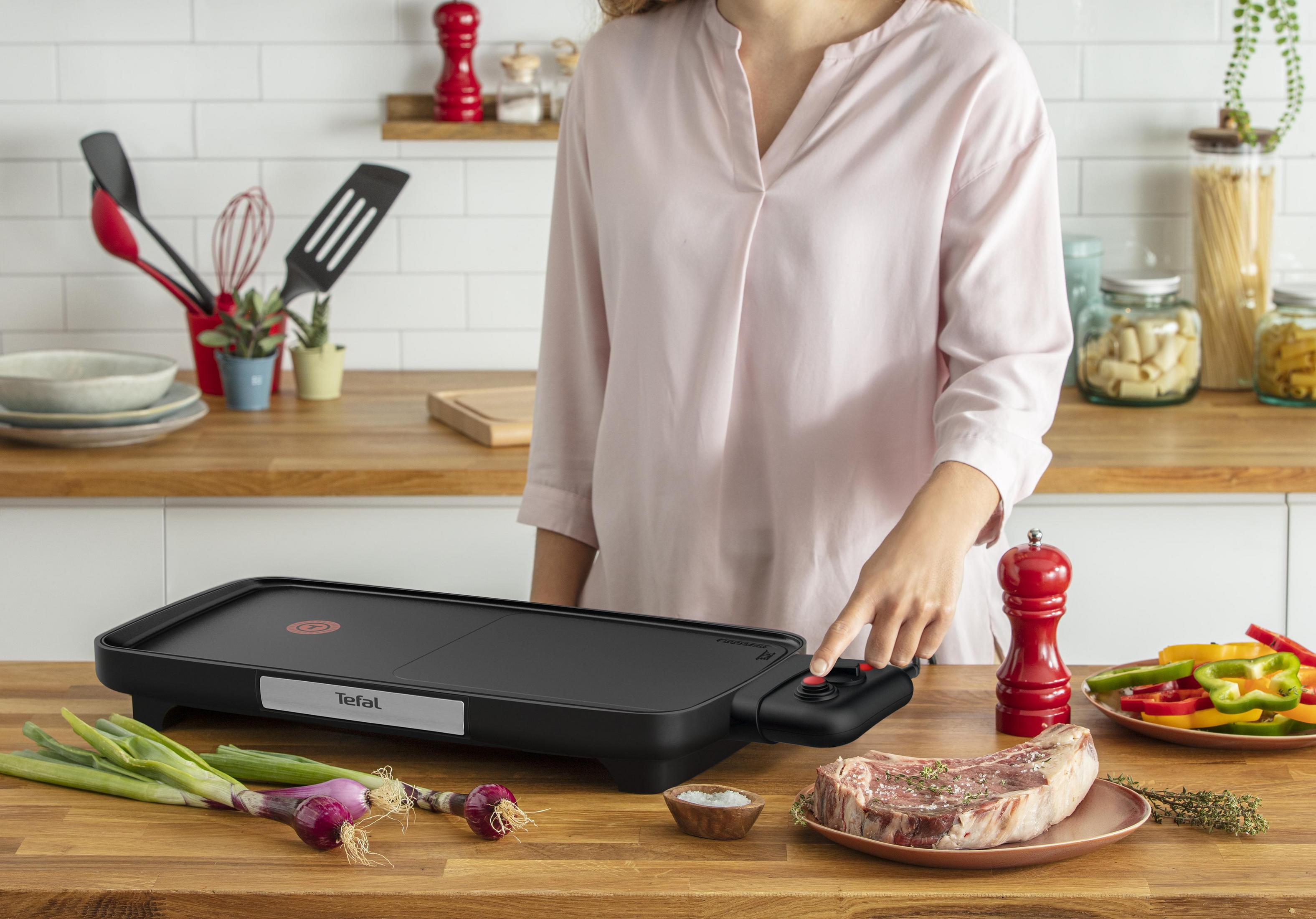 Frau bedient eine schwarze Grillplatte mit Essen und Zutaten.