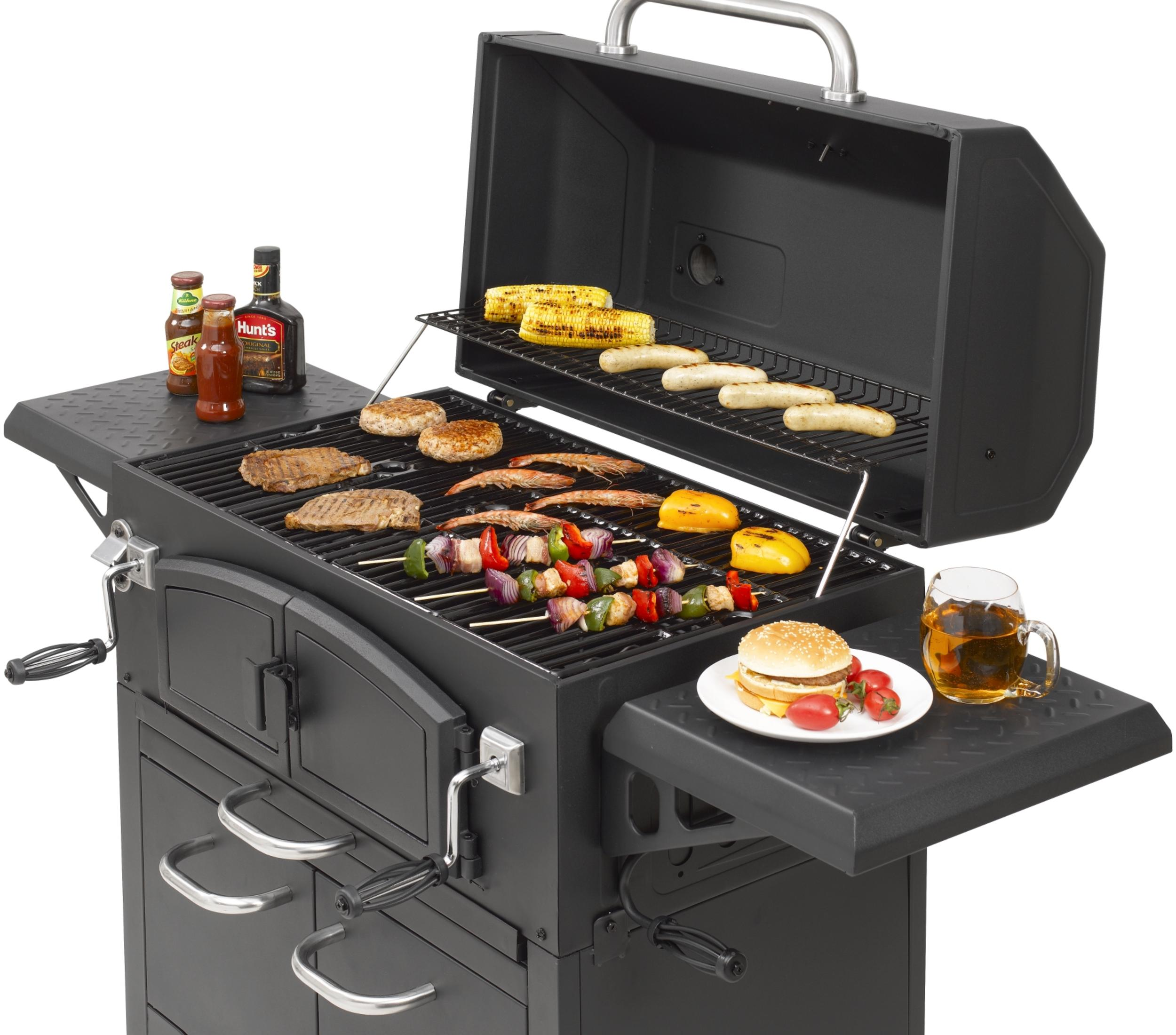 Schwarzer Holzkohlegrill mit Essen auf dem Grill. Saucenflaschen und ein Bierkrug stehen daneben.