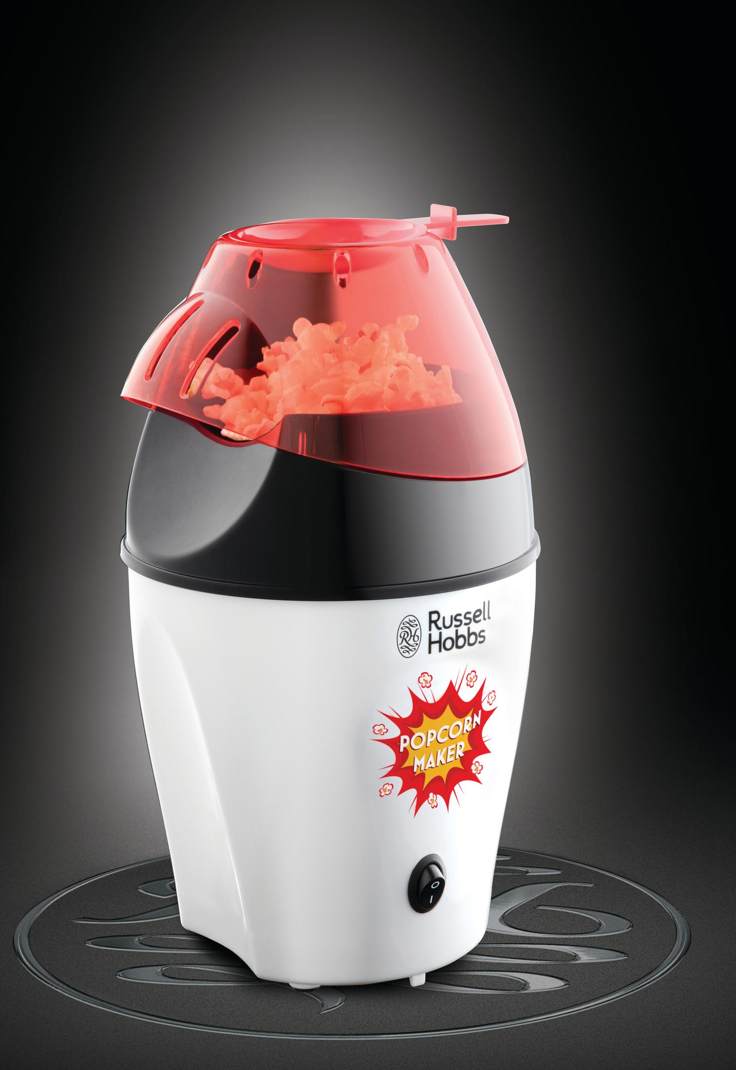 Weißer Russell Hobbs Popcorn-Maker mit rotem Deckel, gefüllt mit Popcorn, auf dunkler Oberfläche.