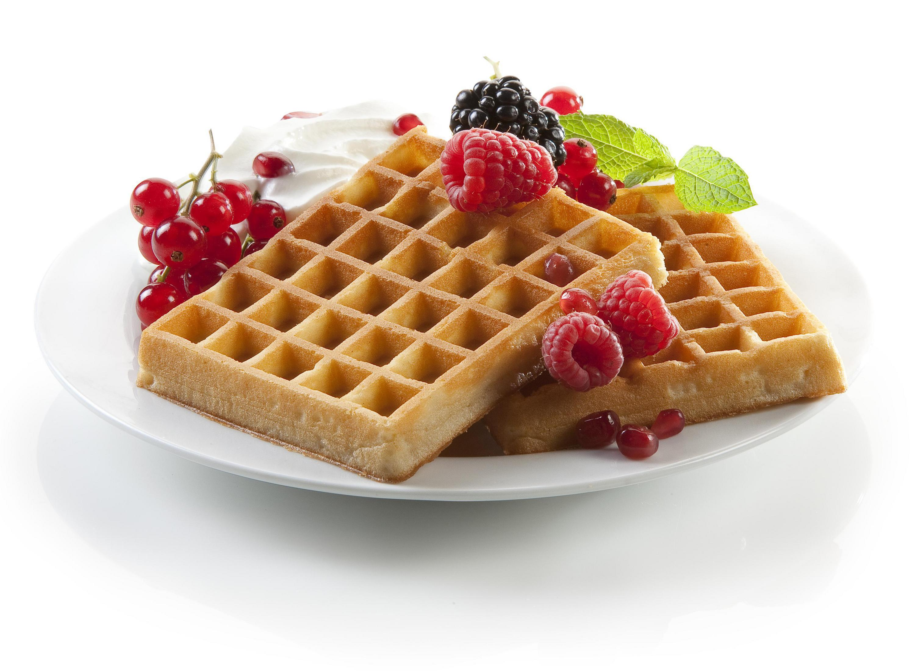 Gofry na talerzu z bitą śmietaną, malinami, jeżynami i czerwonymi porzeczkami.