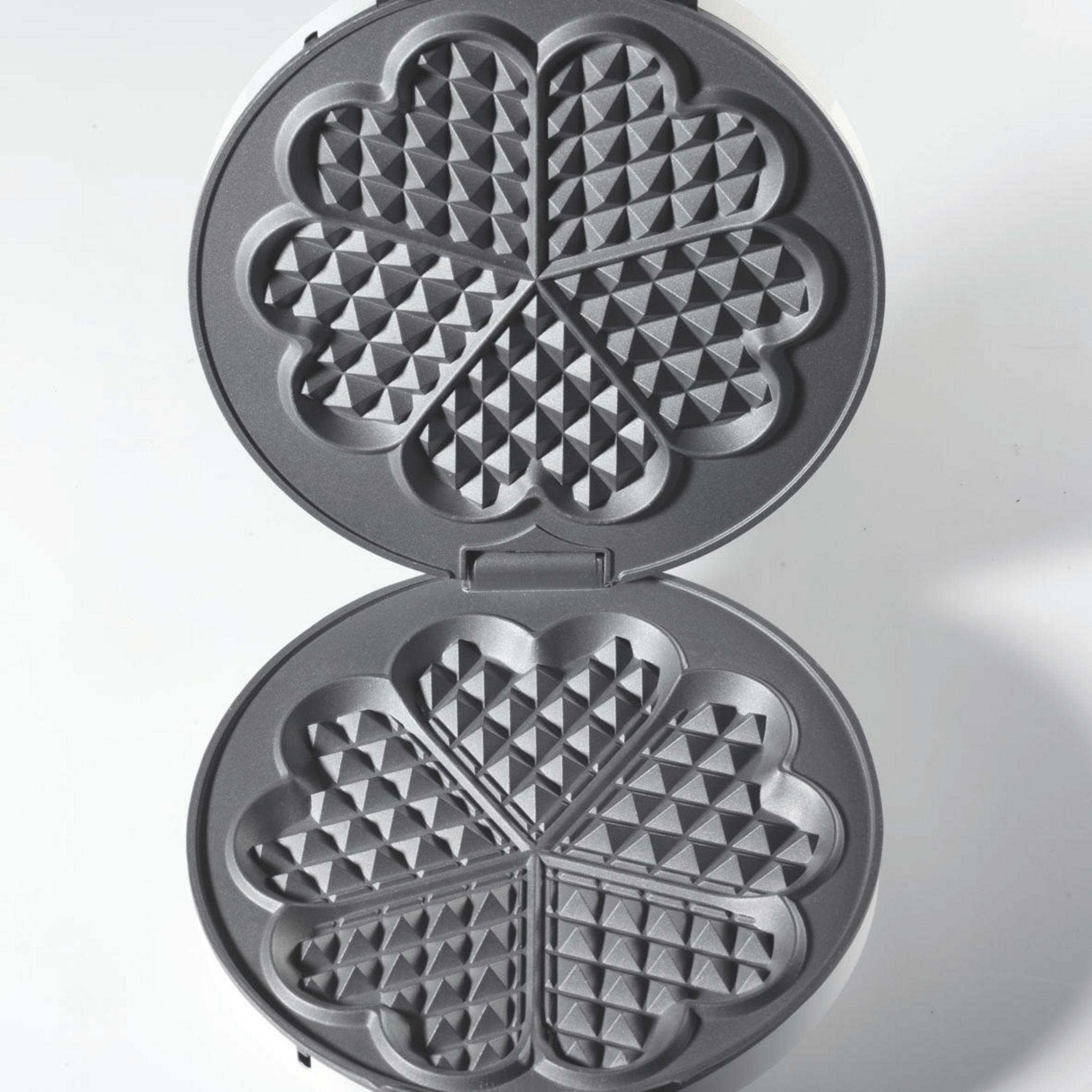 Otwarta gofrownica, pokazująca formy w kształcie serca na białym tle.