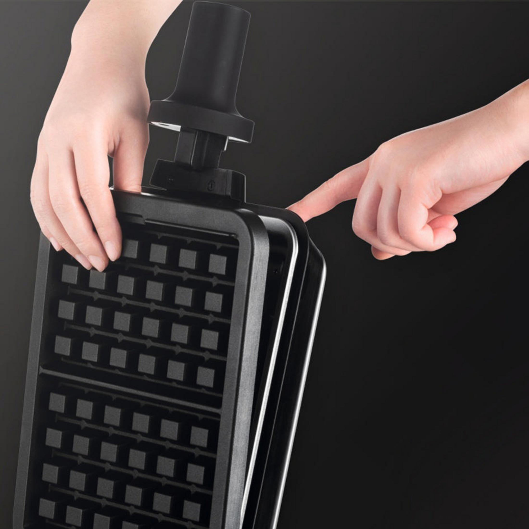 Dłonie obsługują czarny gofrownicę, zamykając pokrywę.