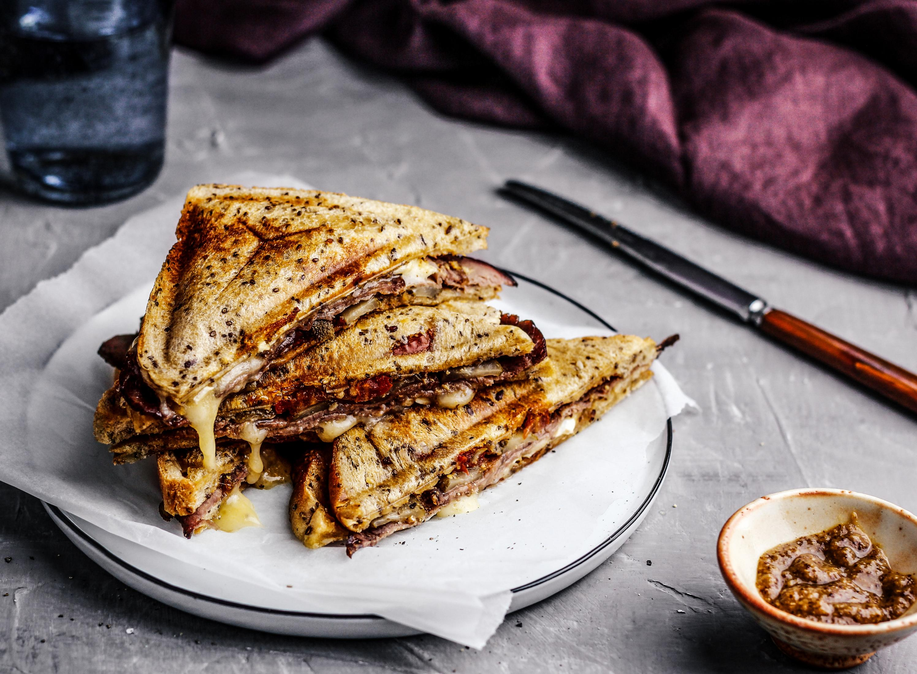 Talerz z dwiema połówkami kanapki z roztopionym serem, małą miseczką sosu i szklanką wody.