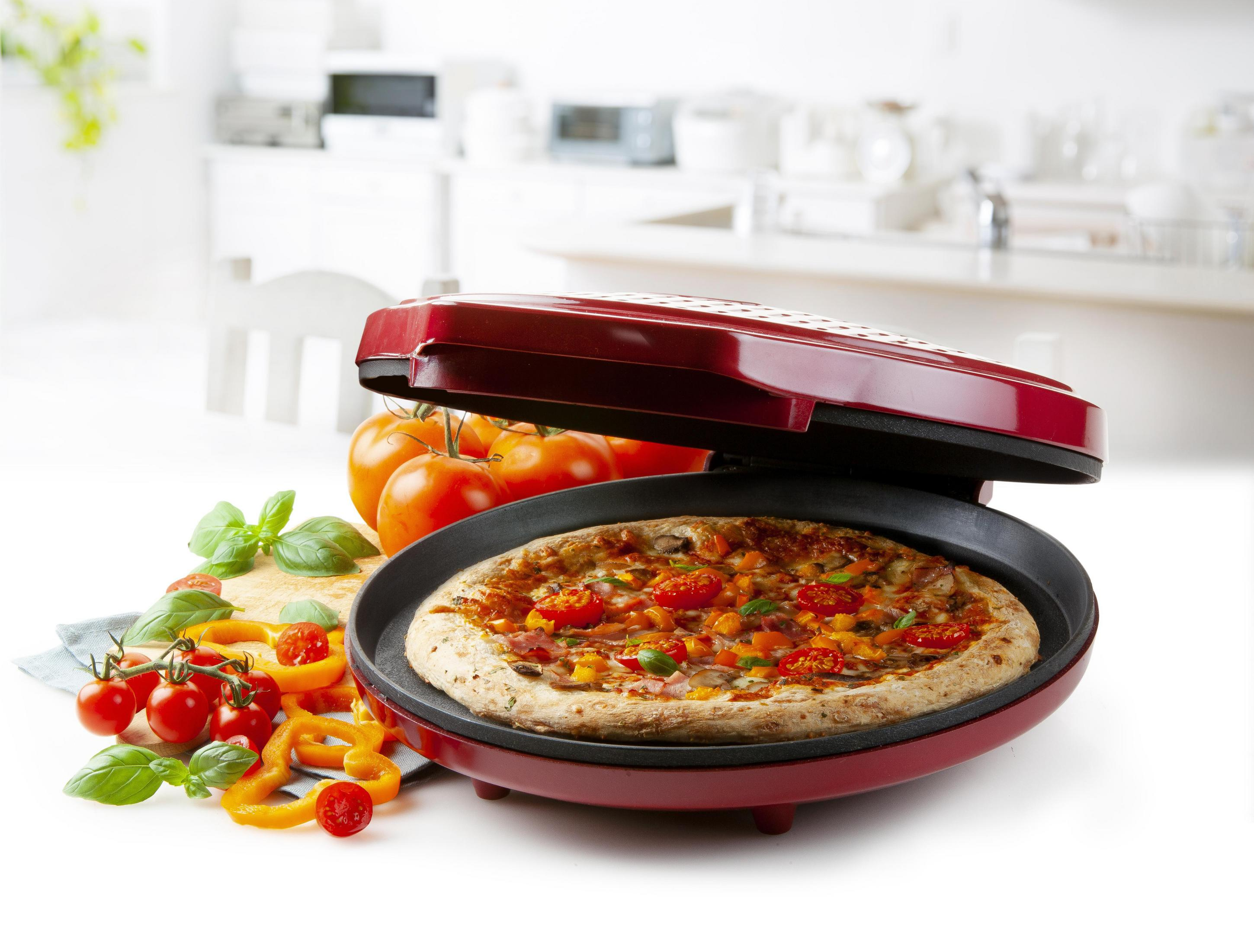 Una máquina para hacer pizza con una pizza dentro, rodeada de ingredientes.