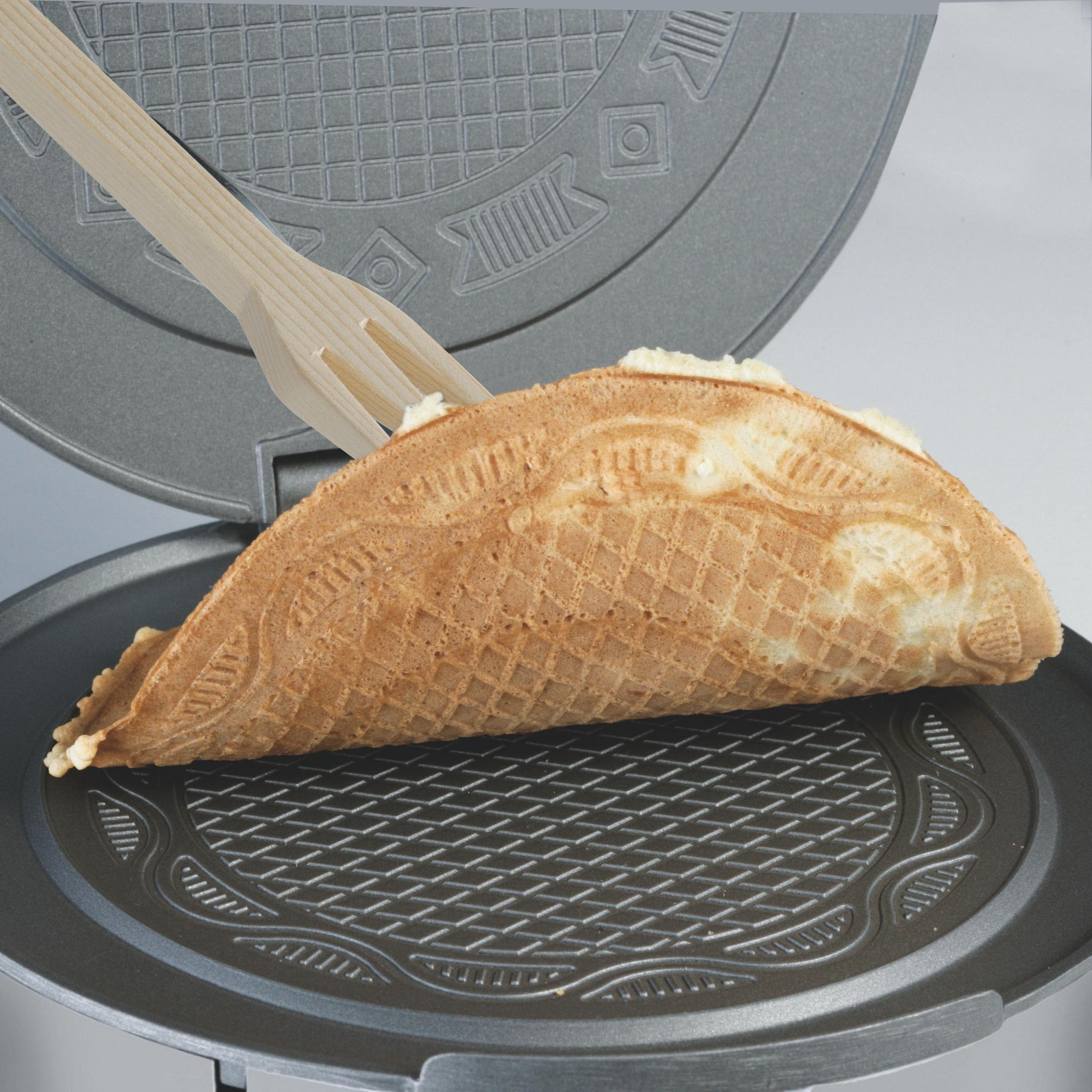 Eine Waffel, die in einem offenen Waffeleisen gehalten wird. Eine Holzgabel hält die Waffel.