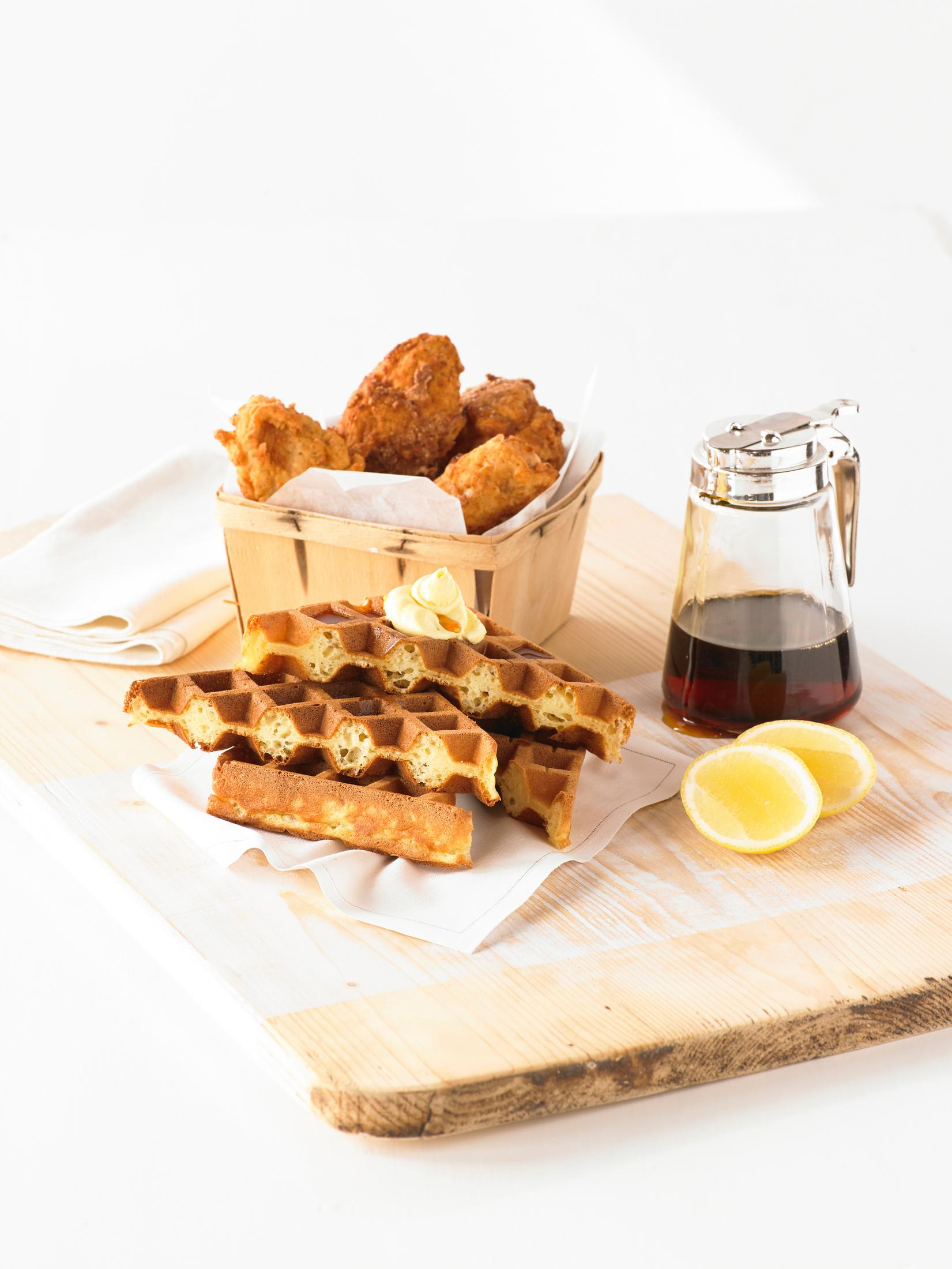 Waffeln, gebratenes Hühnchen, Sirup und Zitrone auf einem Holzbrett. Heller Hintergrund und Essen.