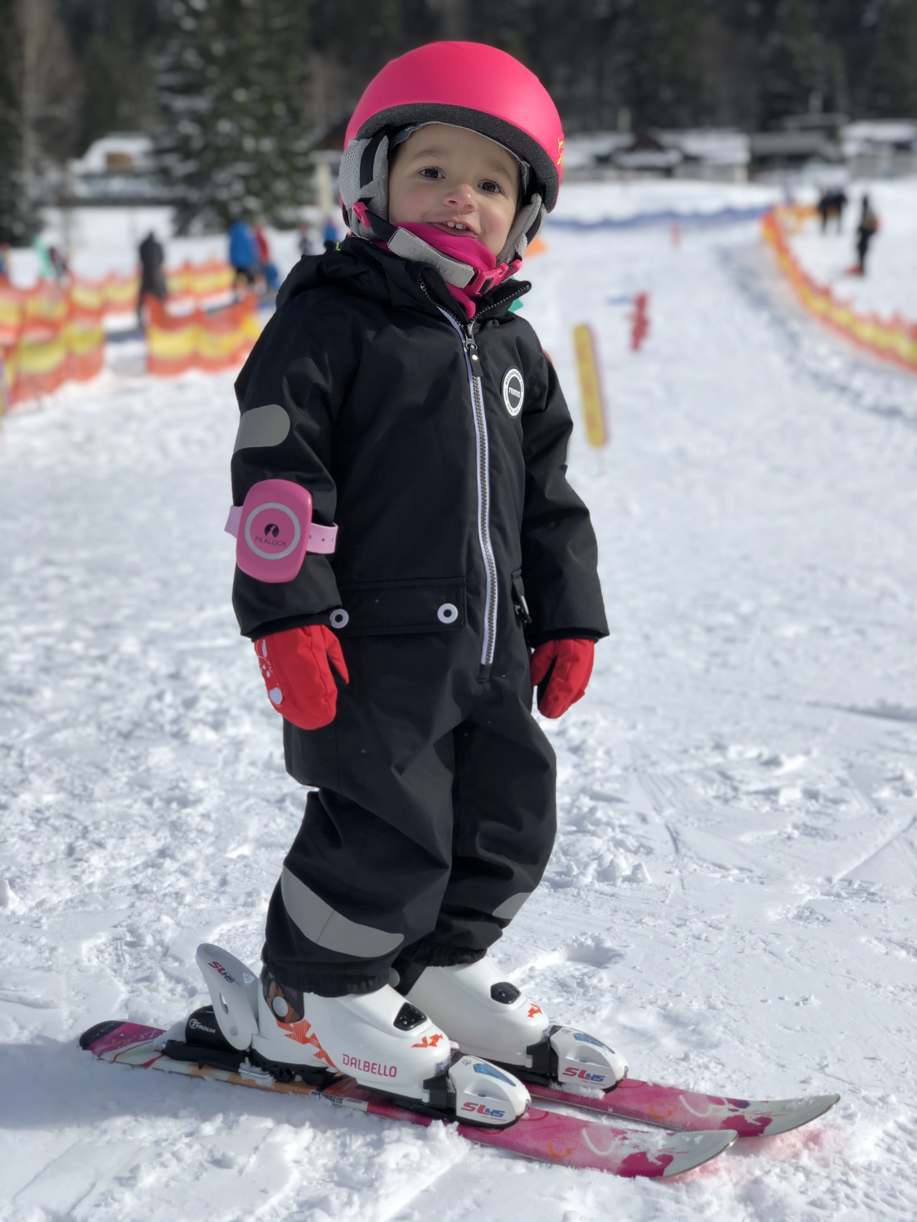 Ein kleines Kind auf Skiern mit rosa Helm und Ausrüstung, bei Schnee.