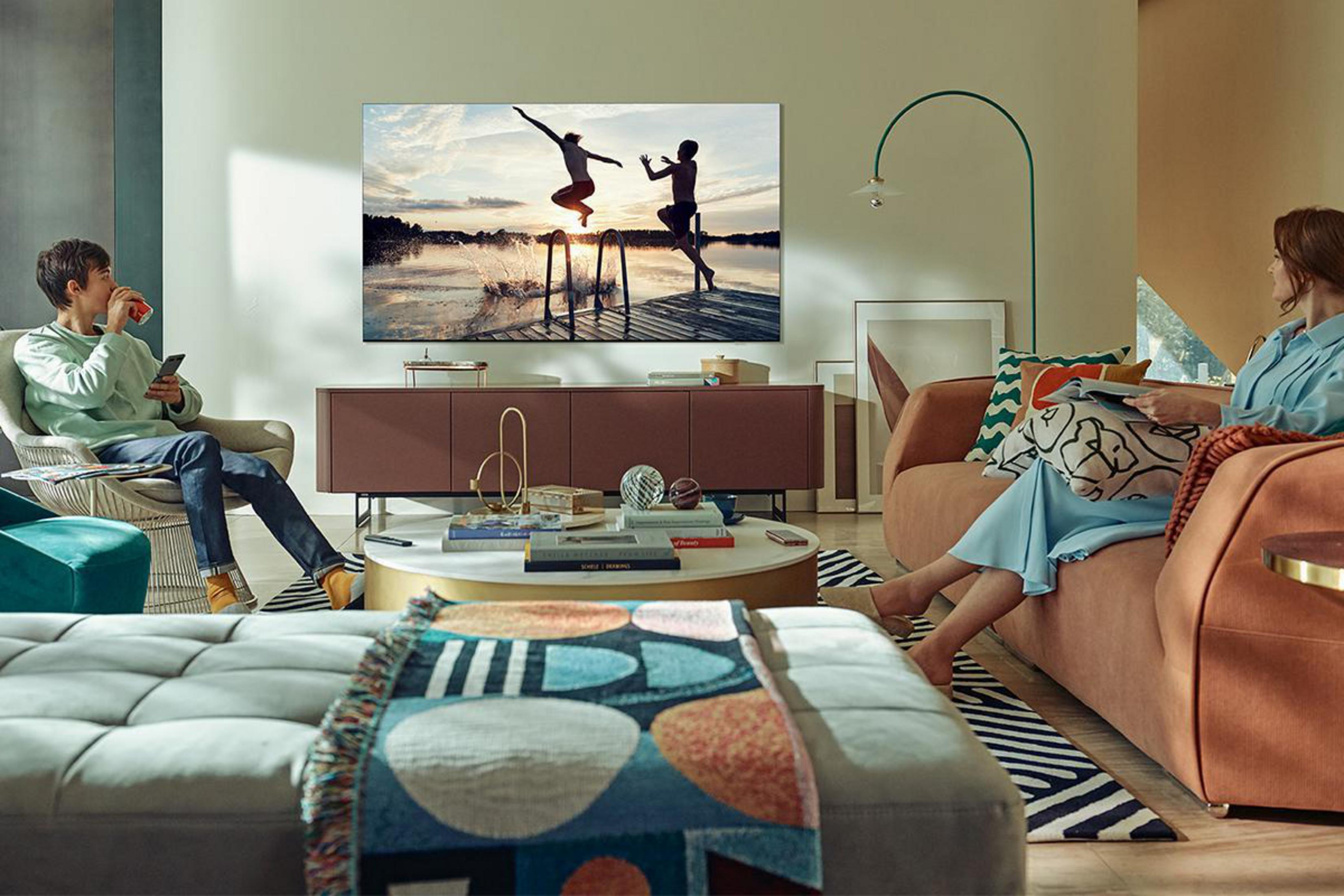 Scena w salonie z telewizorem wyświetlającym ludzi skaczących do wody. Ludzie siedzą na kanapie i krześle.