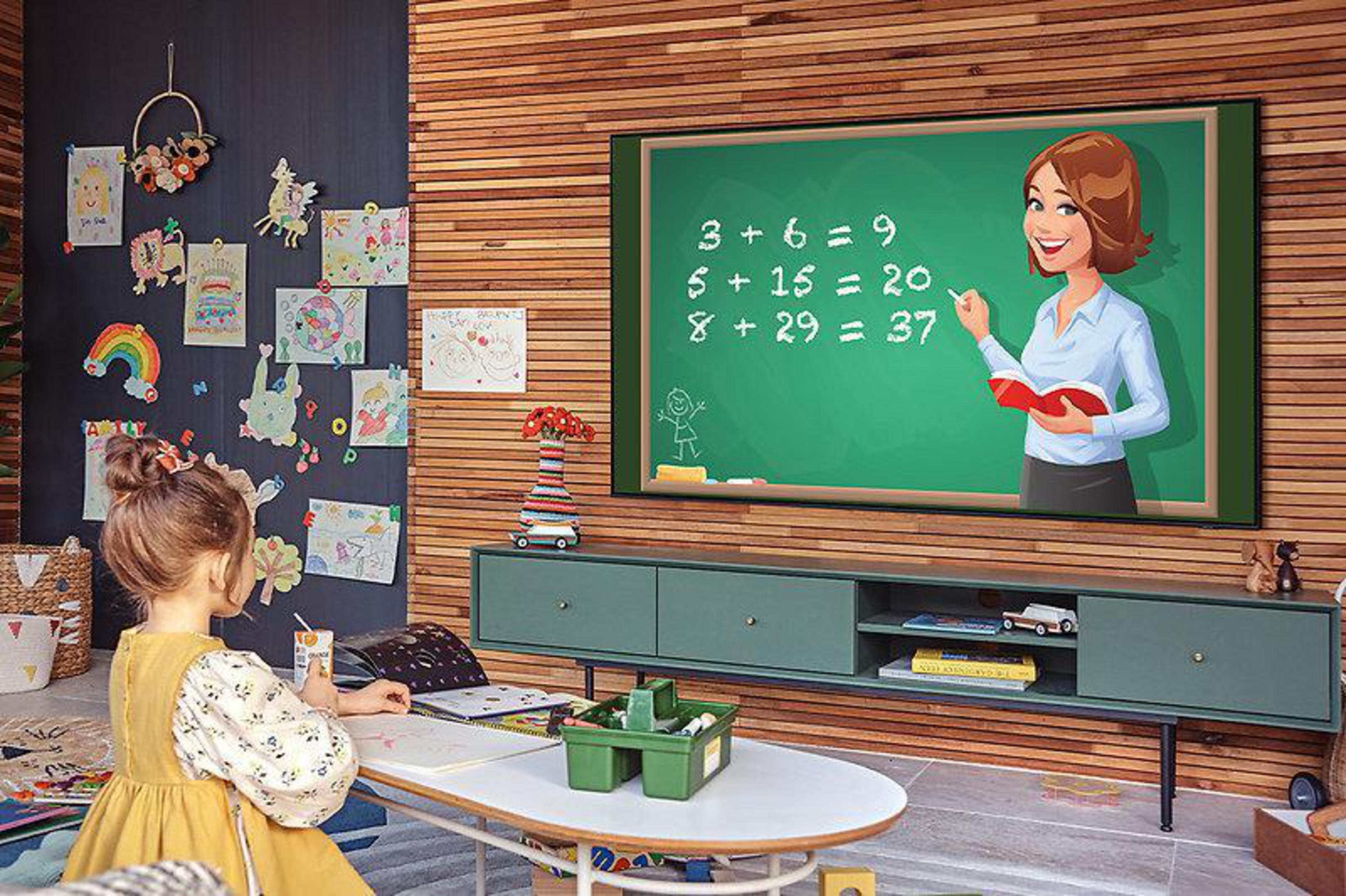 Dziewczynka siedzi, oglądając ekran TV. Nauczycielka na ekranie, uczy matematyki. Pokój ma rysunki, biurko i drewnianą ścianę.