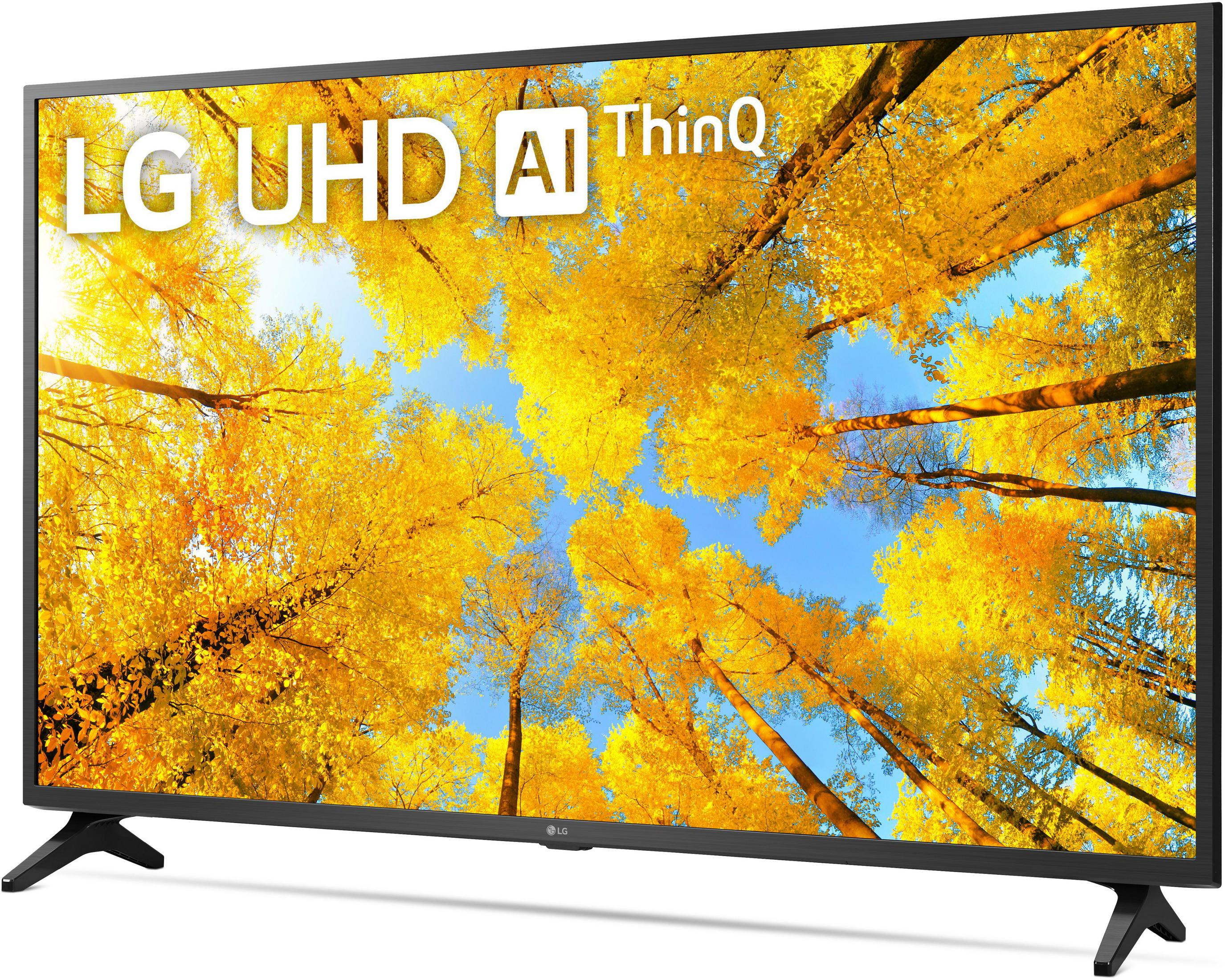 Duży telewizor LG UHD AI ThinQ, pokazujący żółtą scenę jesiennego lasu na tle niebieskiego nieba.