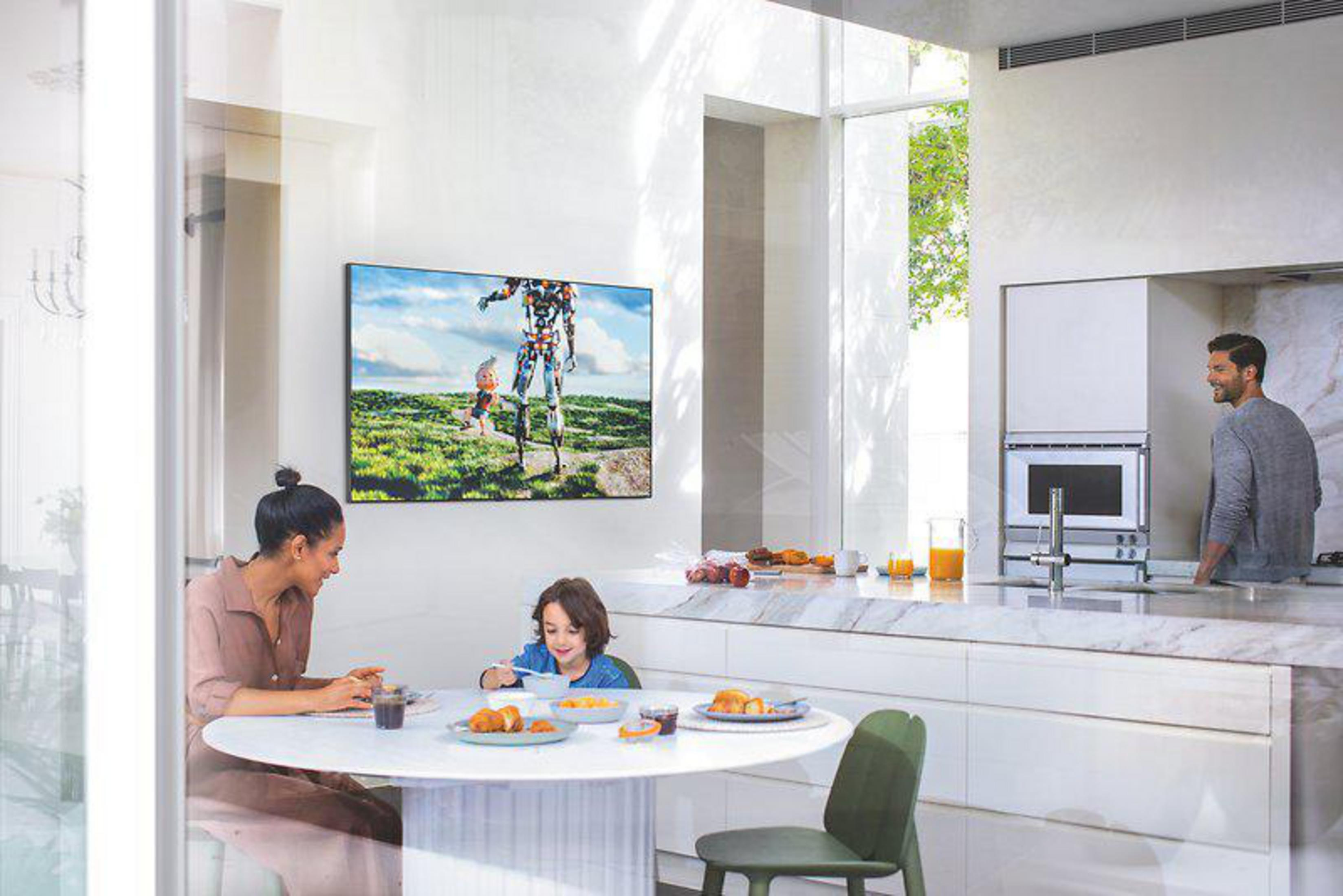 Rodzina jedząca przy okrągłym stole w nowoczesnej kuchni. Telewizor jest zamontowany na ścianie.