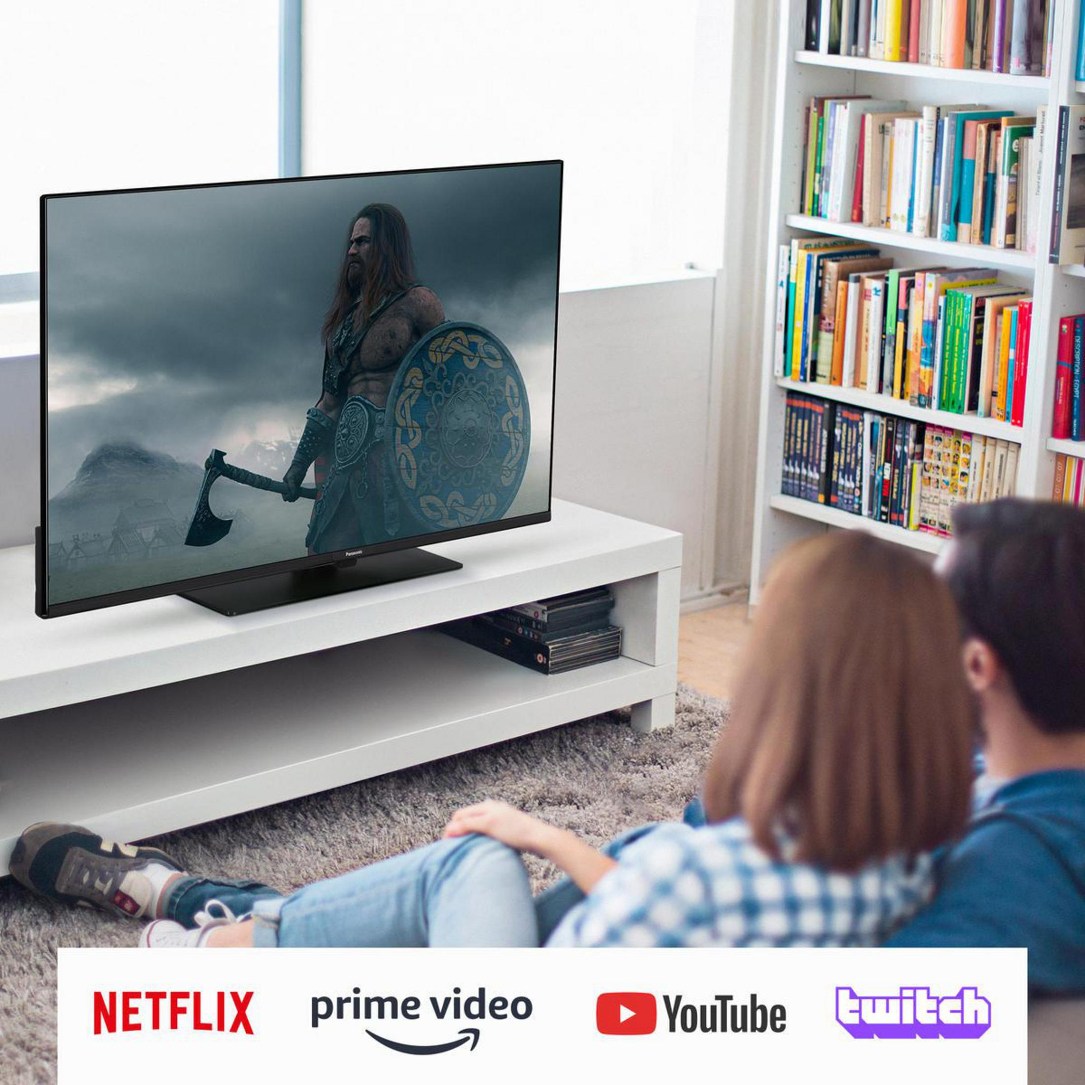 Una coppia seduta su un tappeto, guarda una TV che mostra un vichingo con un'ascia.
