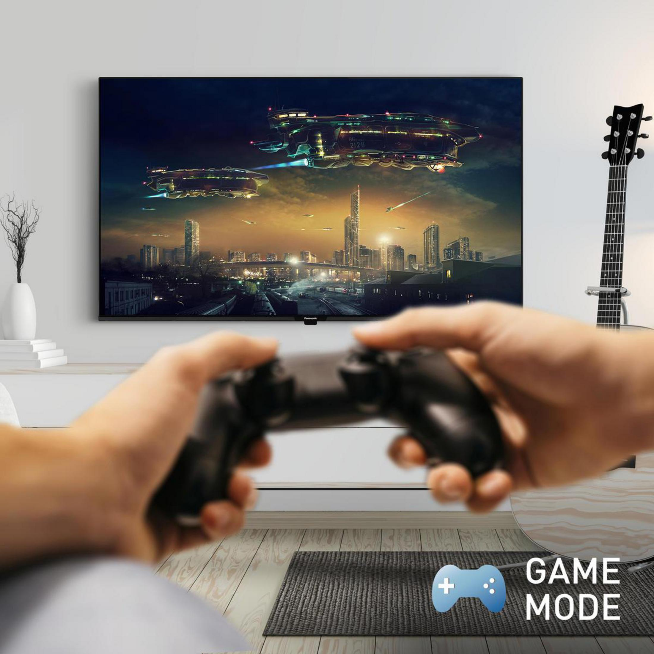 Mani che tengono un controller, TV mostra città futuristica con astronavi.