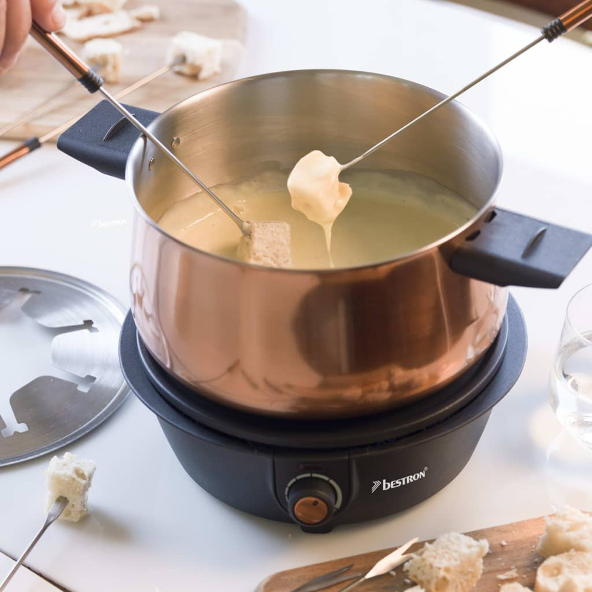 Fondue-Topf mit schmelzendem Käse, mit Brot am Spieß und Bestron-Logo.