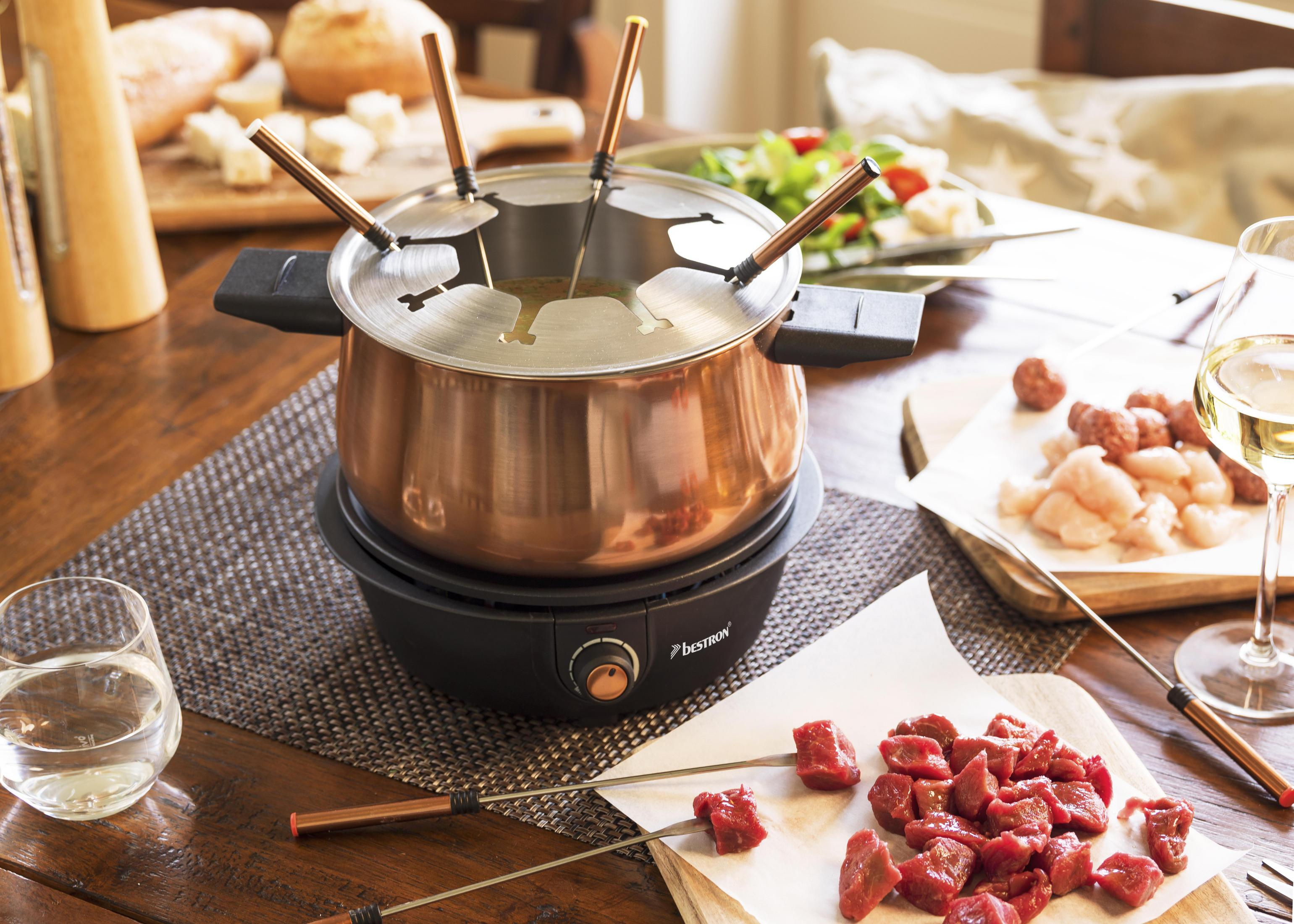 Fondue-Set mit Speisen auf einem Holztisch. Fleisch, Brot, Salat und Getränke.