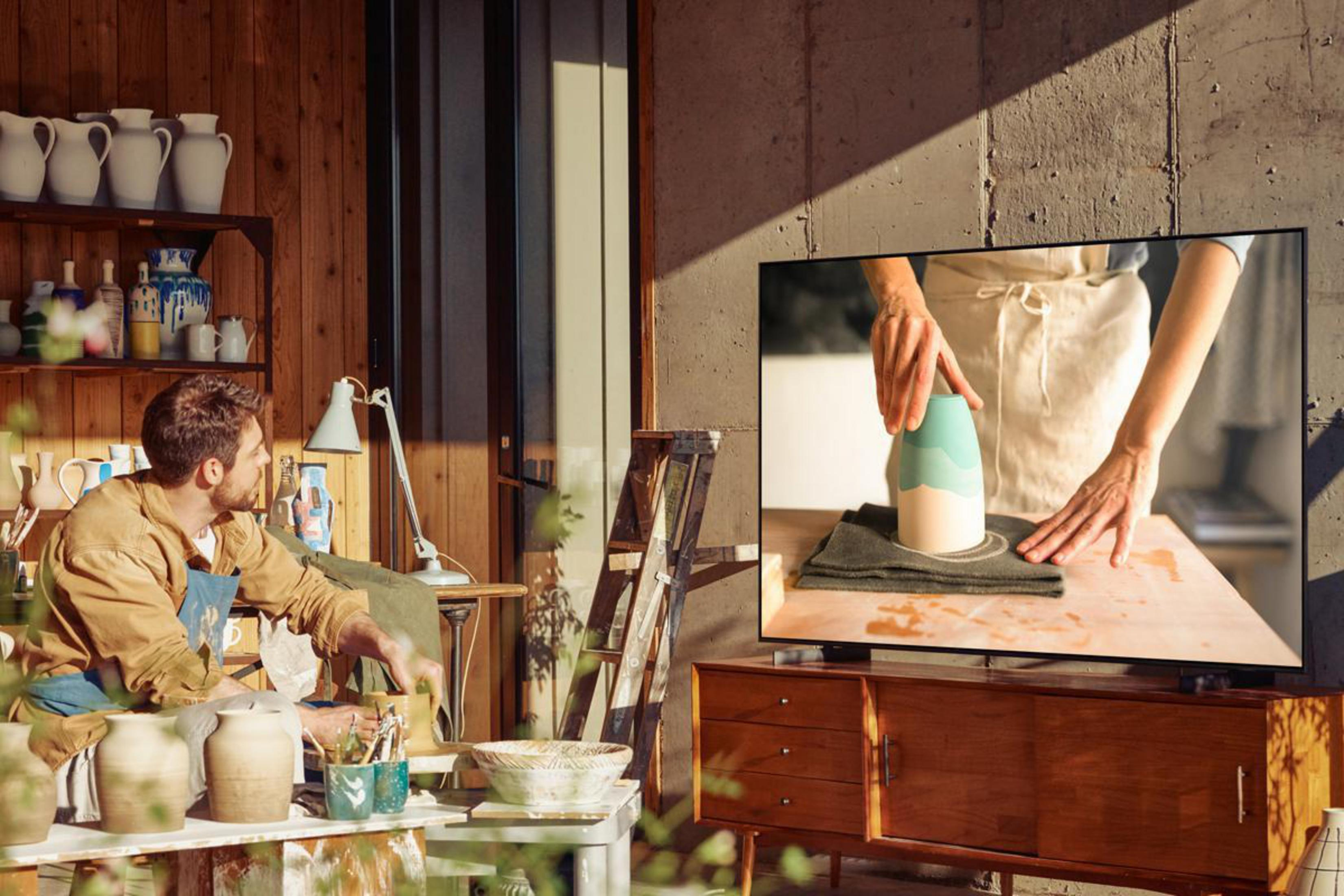 Mężczyzna pracuje z gliną, oglądając telewizor na drewnianej szafce, pokazujący garncarstwo.