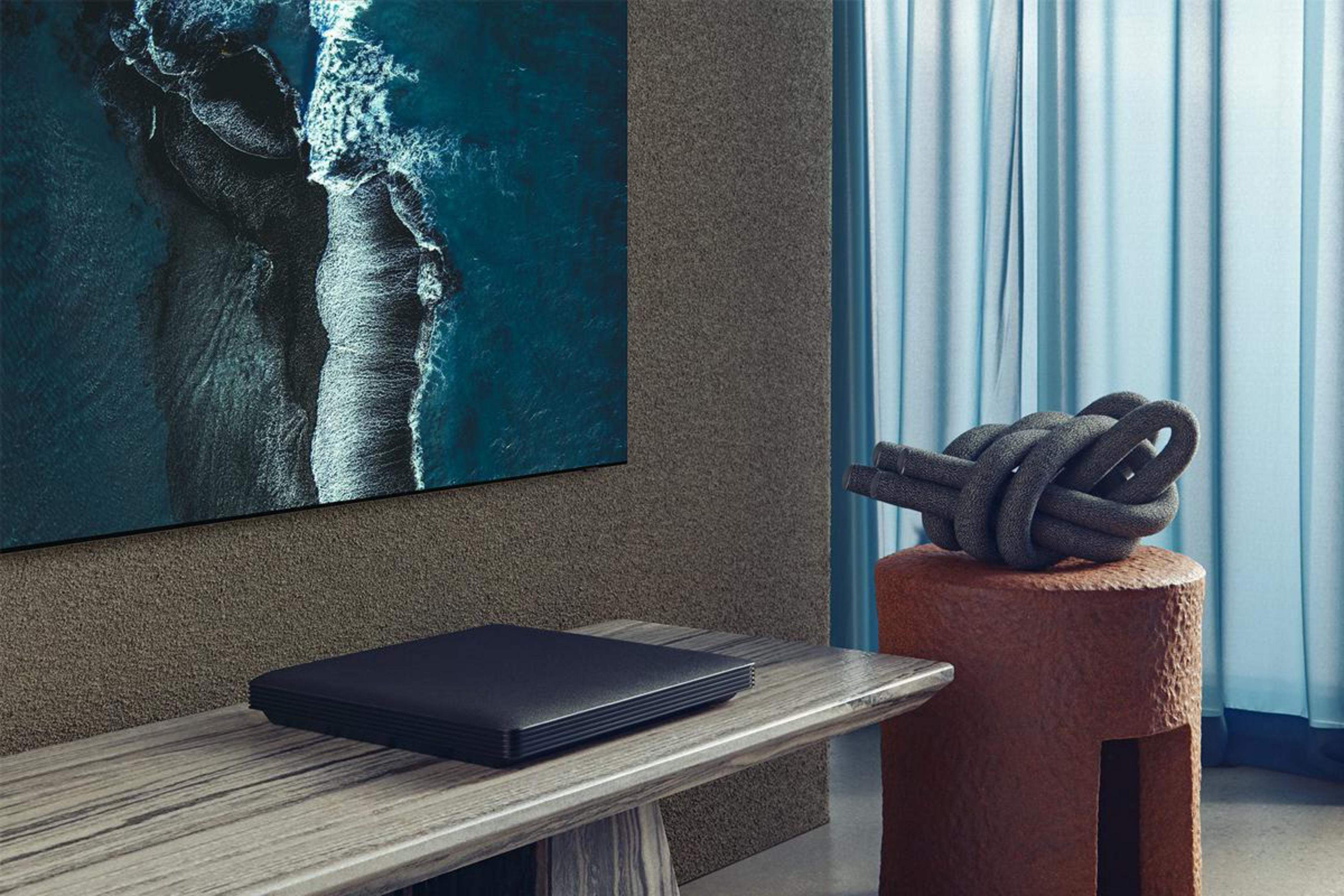 Telewizor nad ławką z czarnym urządzeniem. Dekoracyjny węzeł na brązowej kostce.