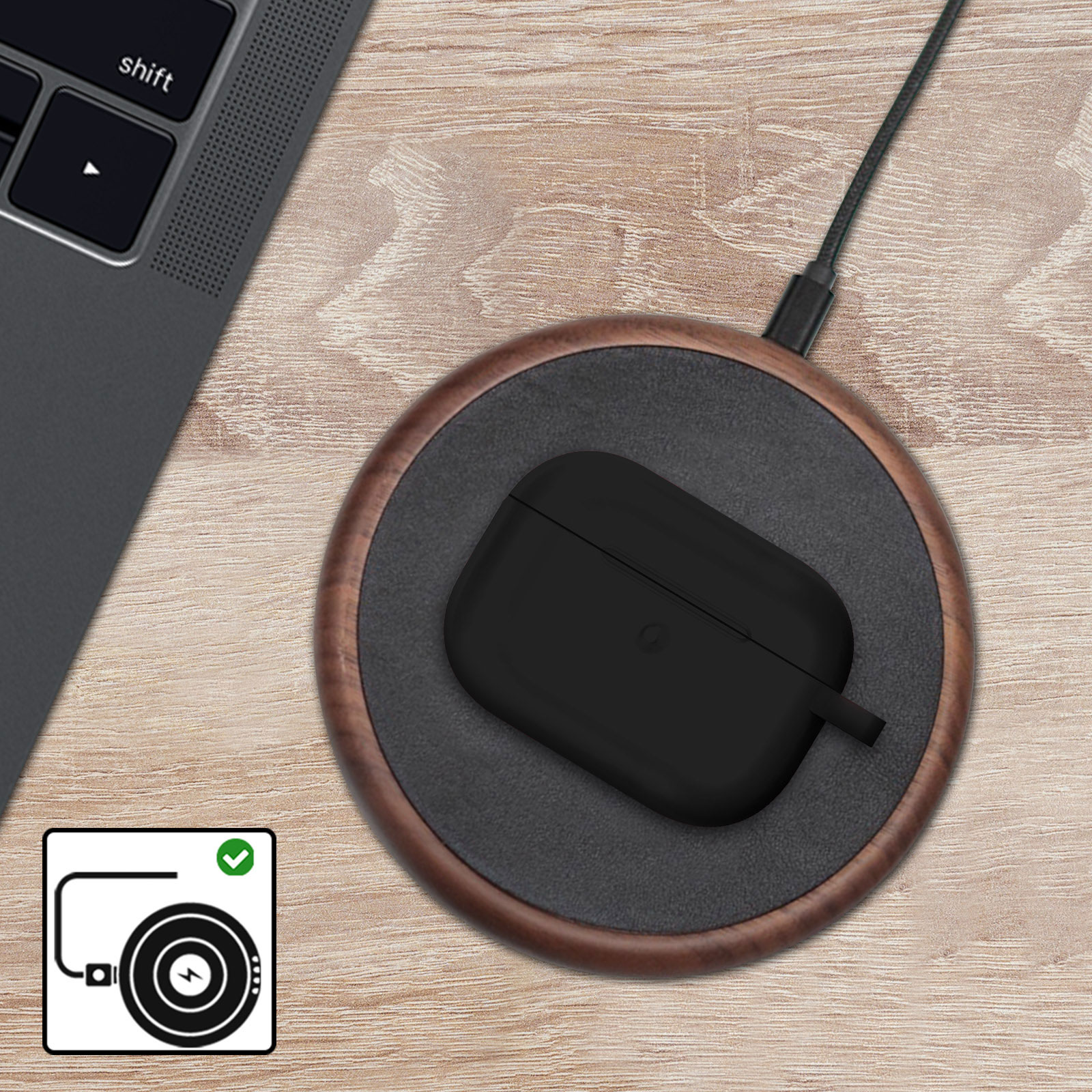 Una funda negra de Airpods en un cargador inalámbrico de madera, con una computadora portátil e indicador de carga.