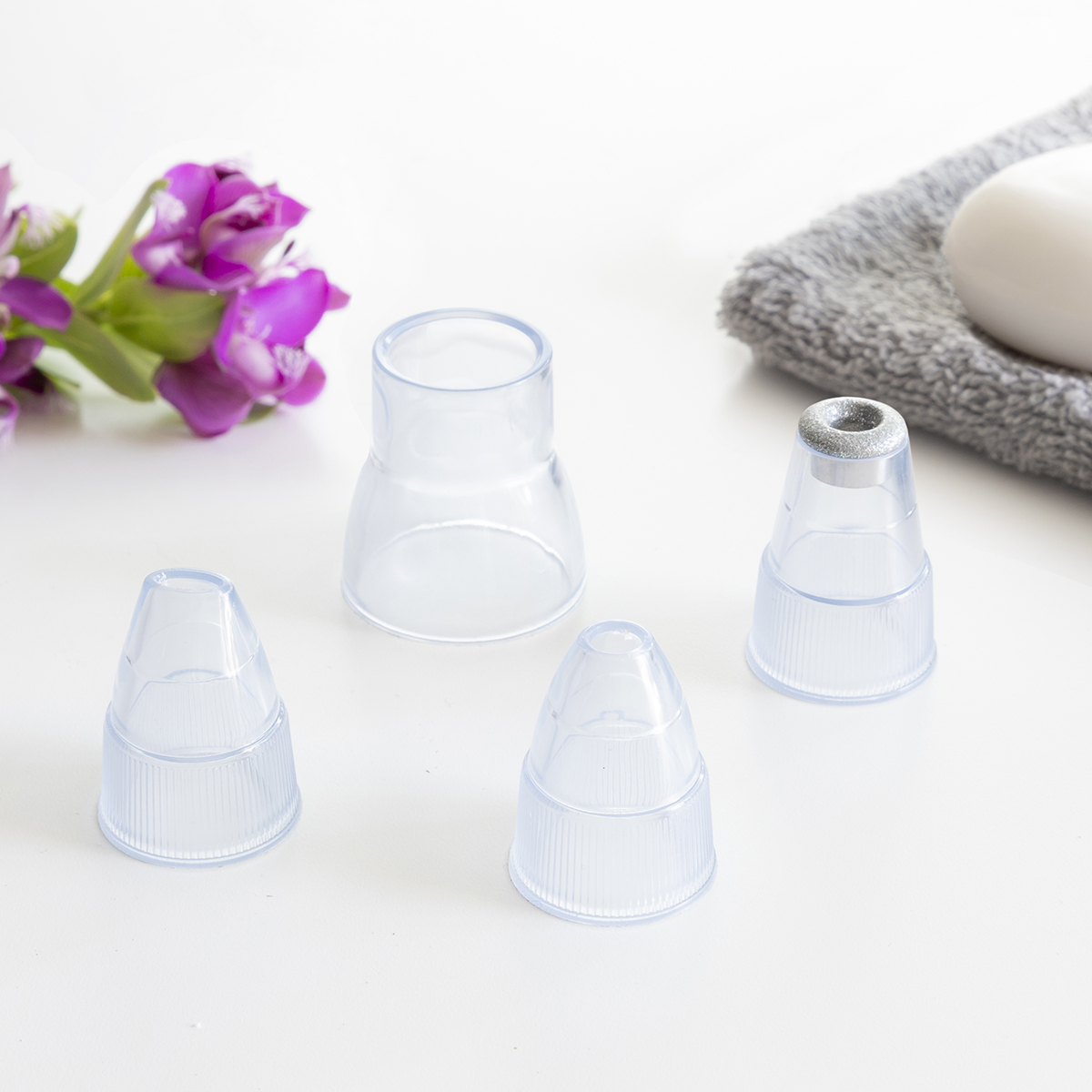 Cuatro accesorios de vacío de poros de plástico transparente, con una flor y una toalla gris.