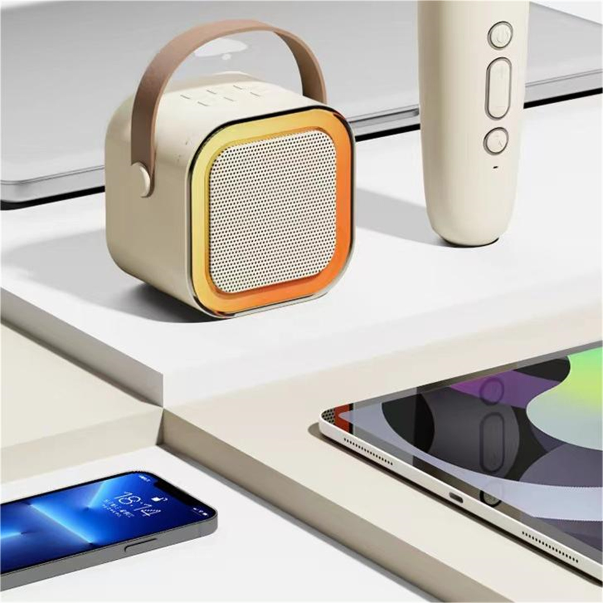 Altavoz, mando a distancia, tableta y teléfono sobre una superficie blanca. Altavoz beige con naranja y asa.