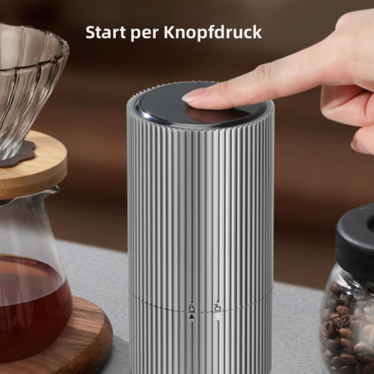 Eine silberne Kaffeemühle mit Knopf. Der Finger einer Person drückt den Knopf zum Starten.