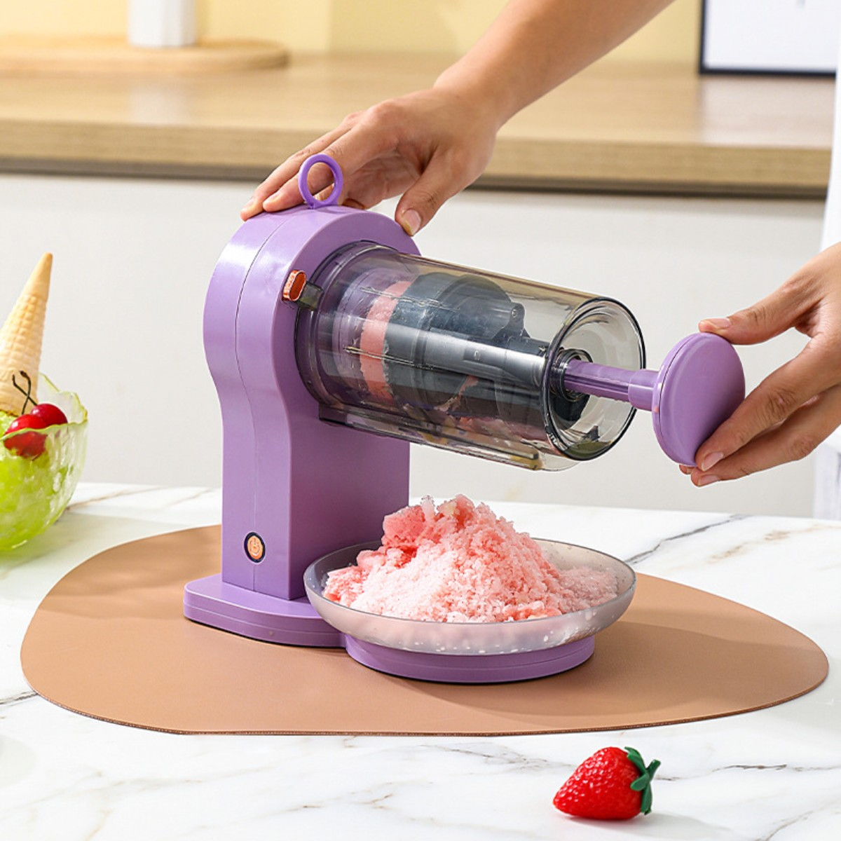Ein lila Eiswürfelbereiter mit Händen, die ihn bedienen, eine Schüssel mit Eis und eine Erdbeere.
