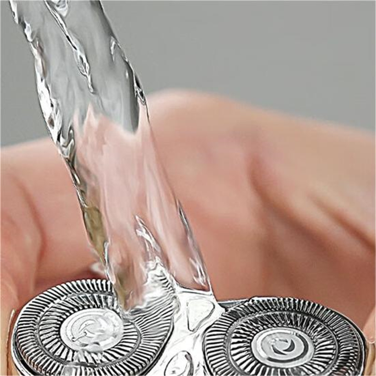 Primer plano del cabezal de una afeitadora eléctrica con agua fluyendo.