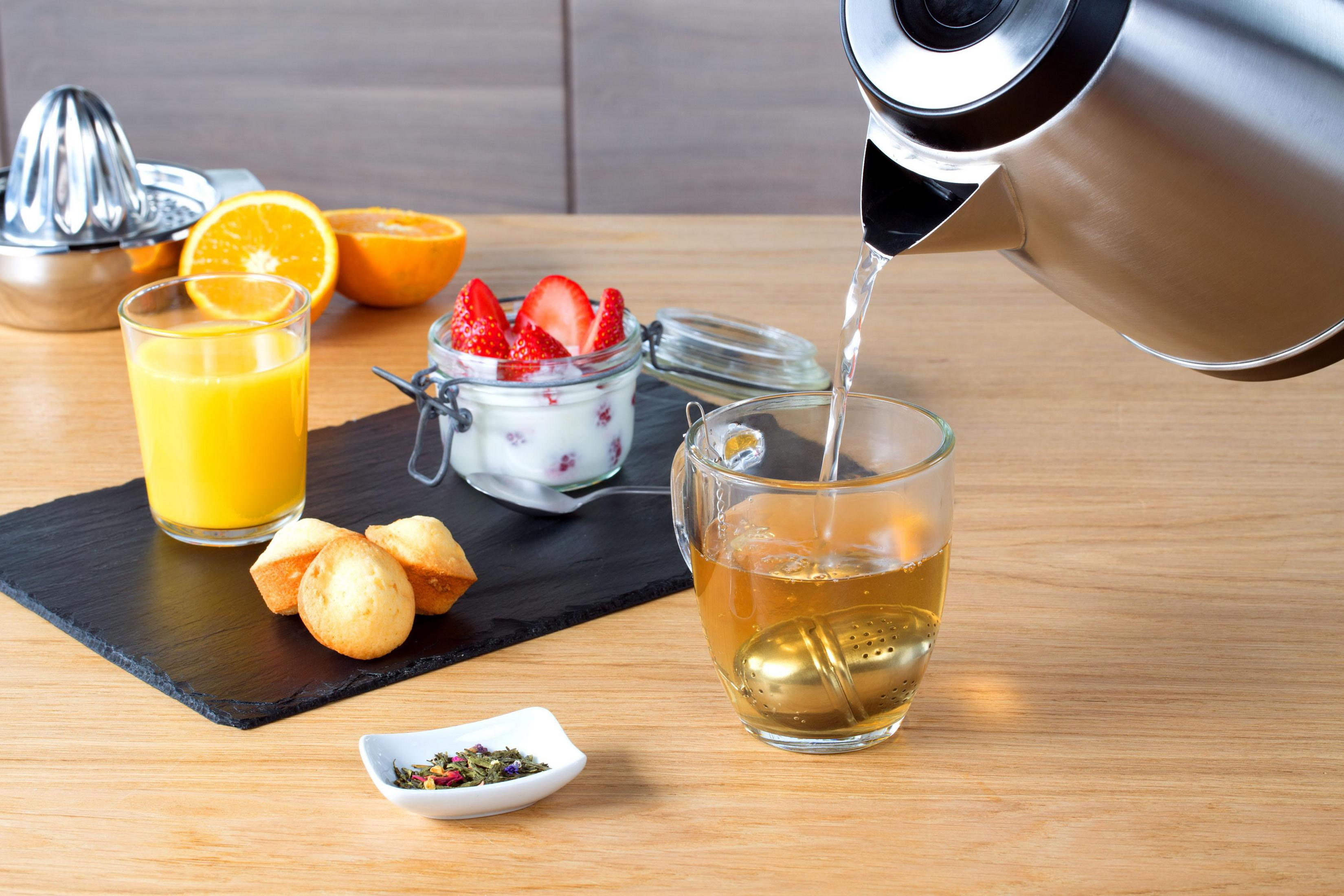 Czajnik nalewa wodę do filiżanki z zaparzaczem do herbaty, plus przekąski.