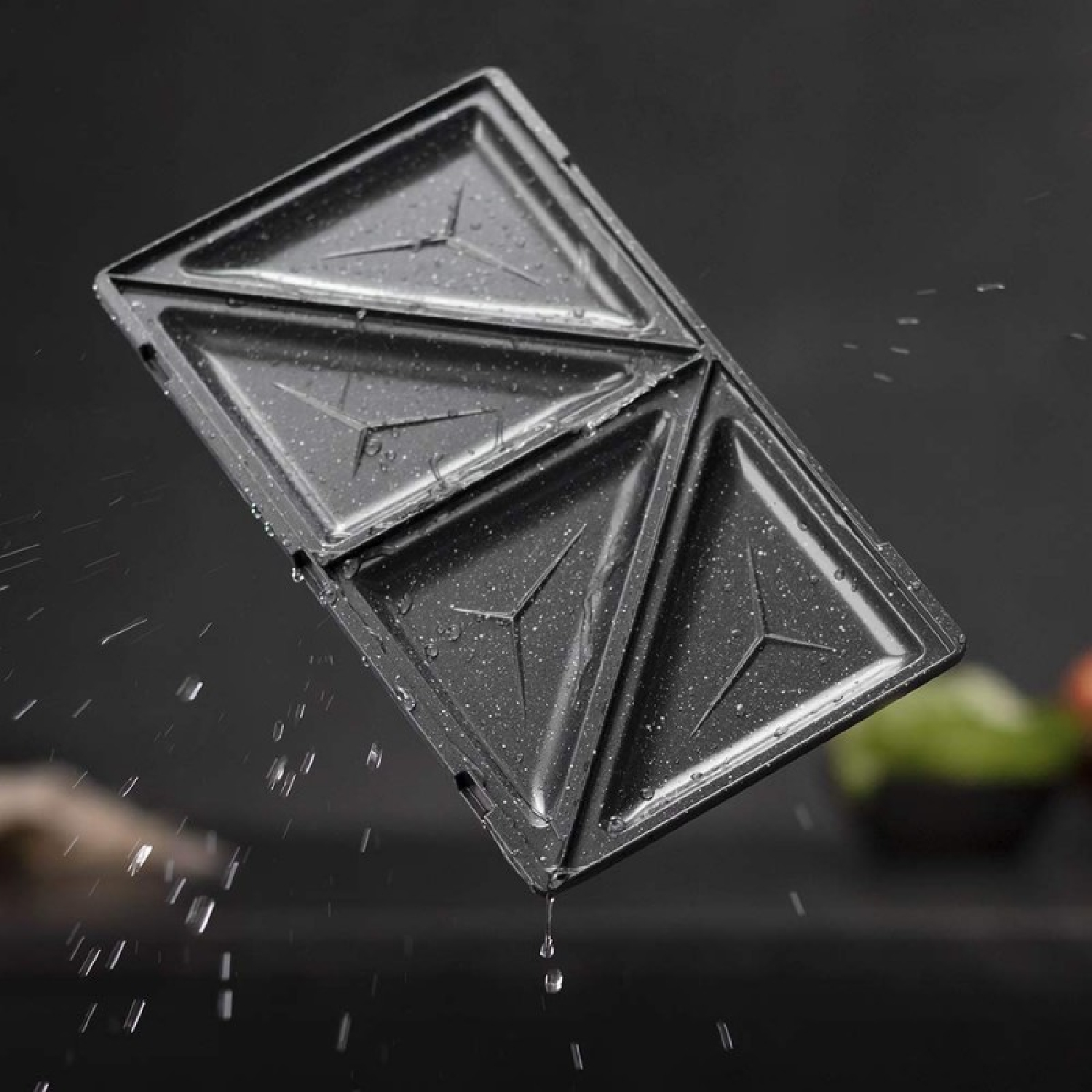 Sandwichiera triangolare con goccioline d'acqua e sfondo scuro.