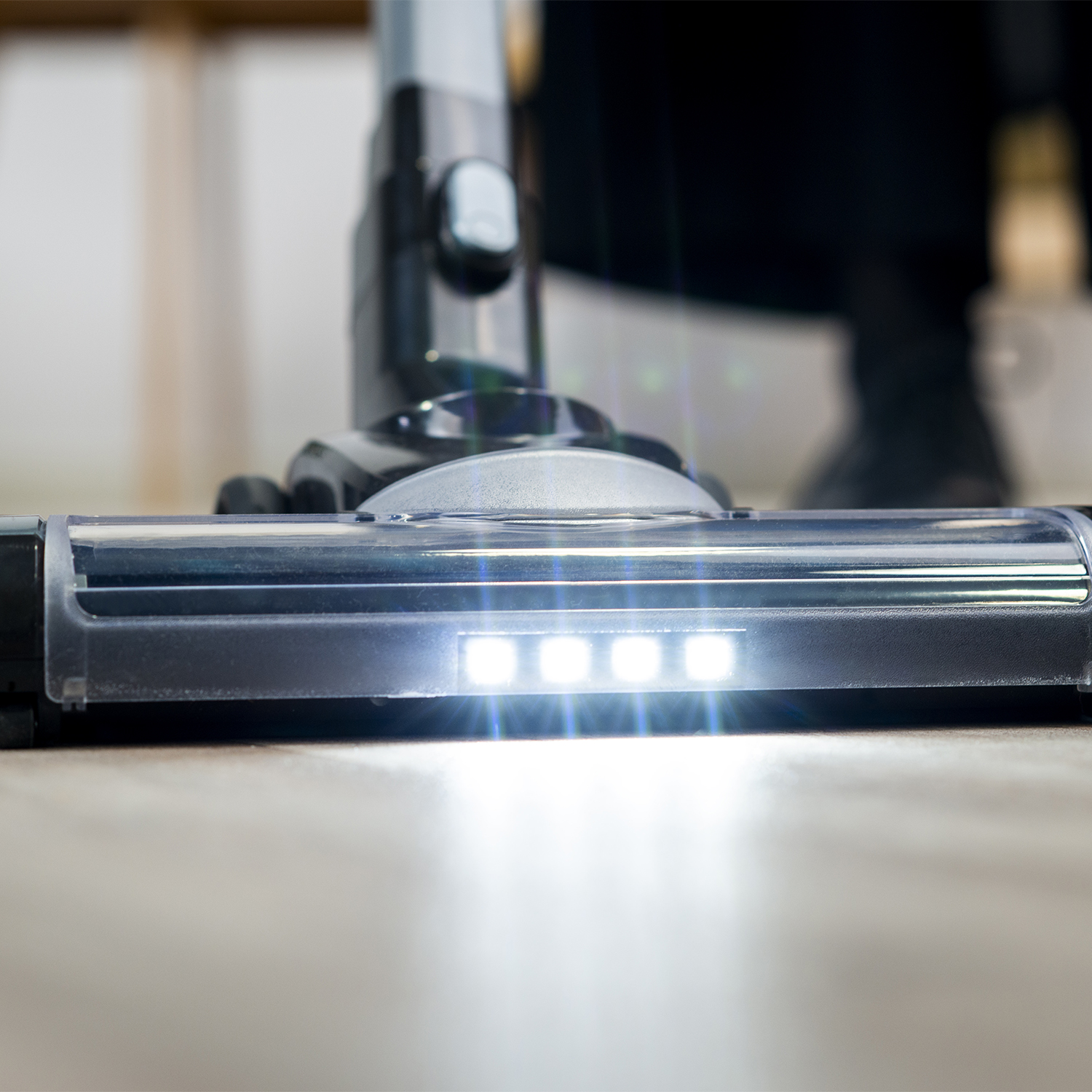 Cabezal de aspiradora con luces LED brillantes, limpiando un piso de madera, toma de primer plano.
