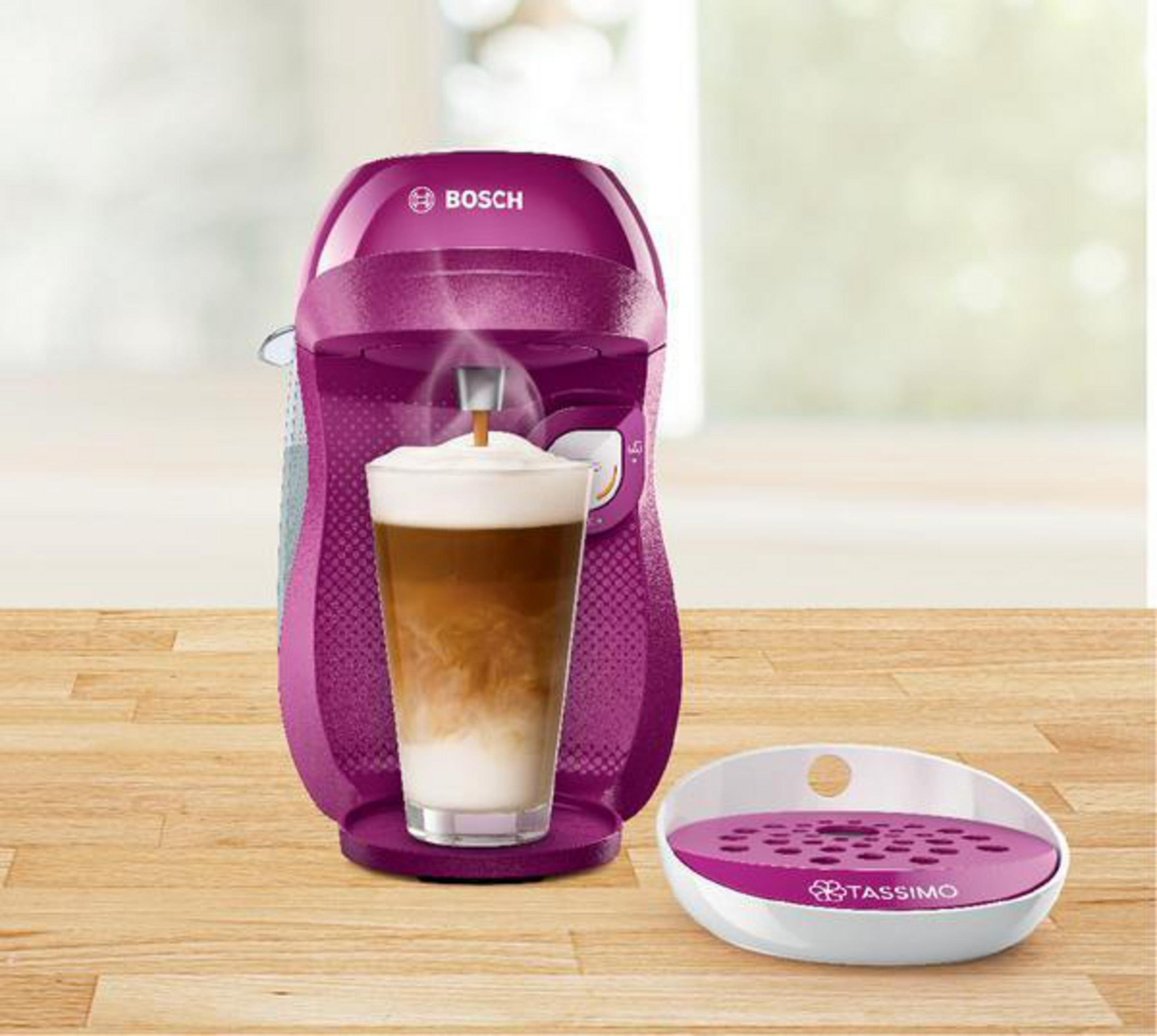 Macchina da caffè viola che eroga caffè in un bicchiere con schiuma di latte e vassoio.